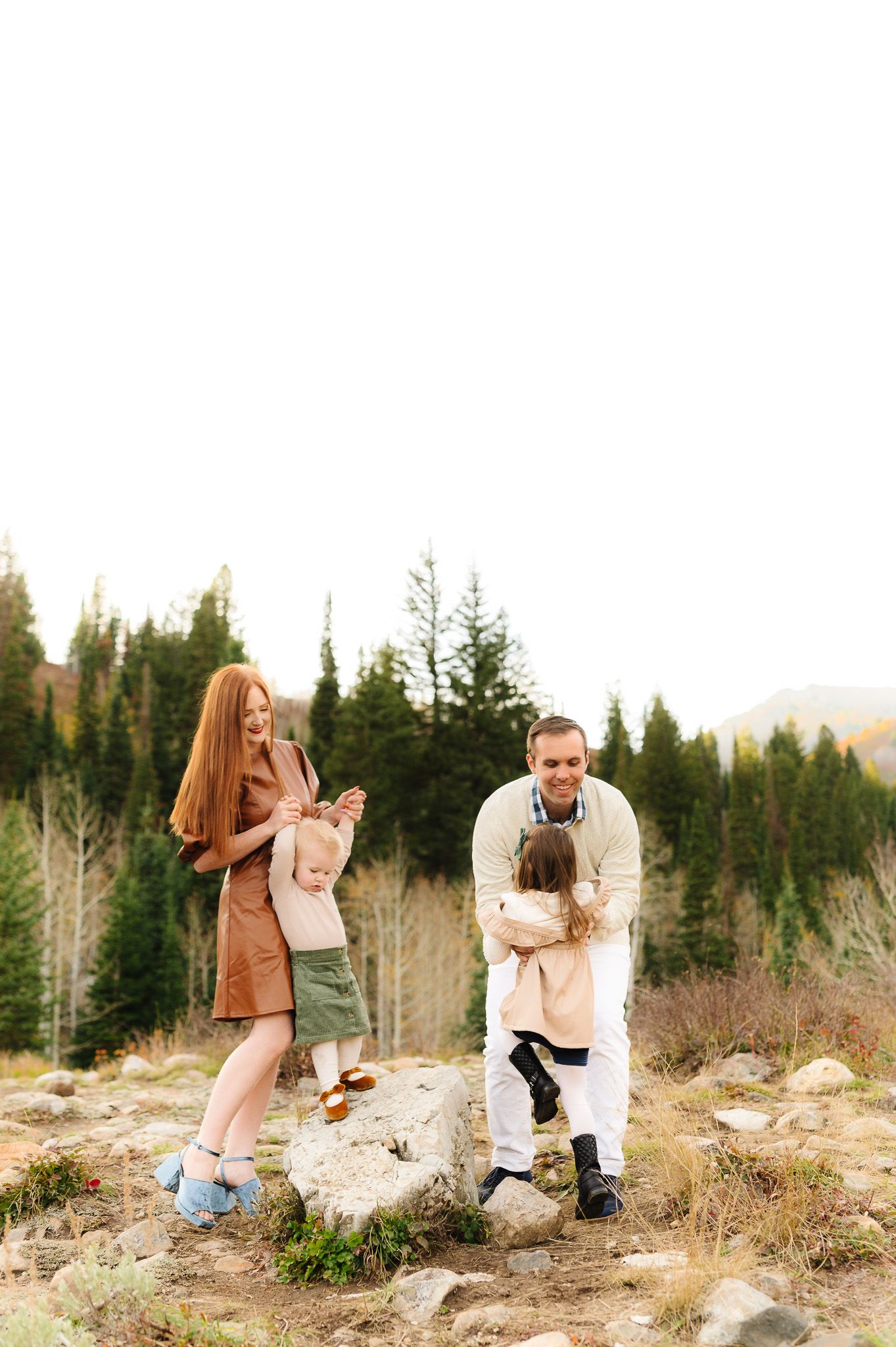A family enjoying a playful moment on rocky terrain with mountain forest scenery.