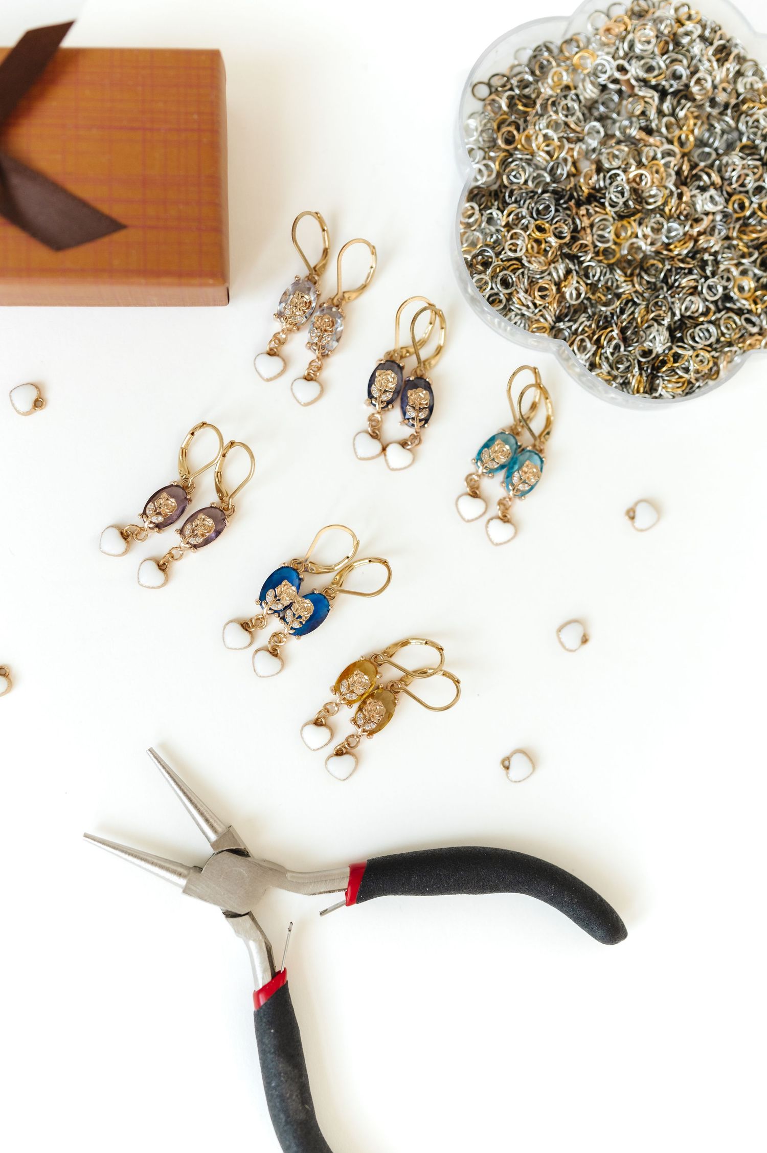 Jewelry making tools and supplies scattered on white surface with pliers visible.
