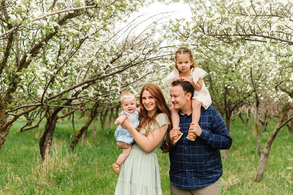 A family shares joyful moments together under flowering trees in a spring orchard setting.