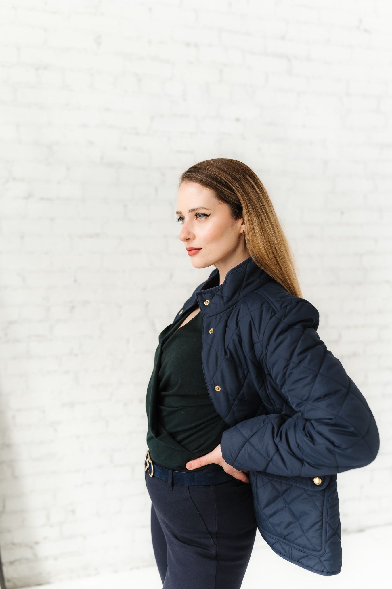 Professional wearing navy quilted jacket poses against white brick wall.