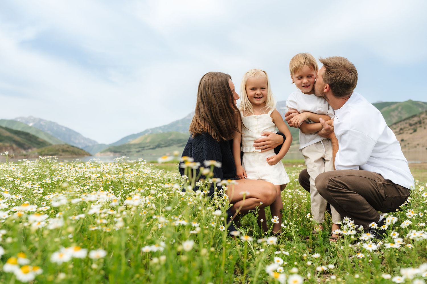 A couple shares an intimate moment in a blooming wildflower meadow with mountains in the background.