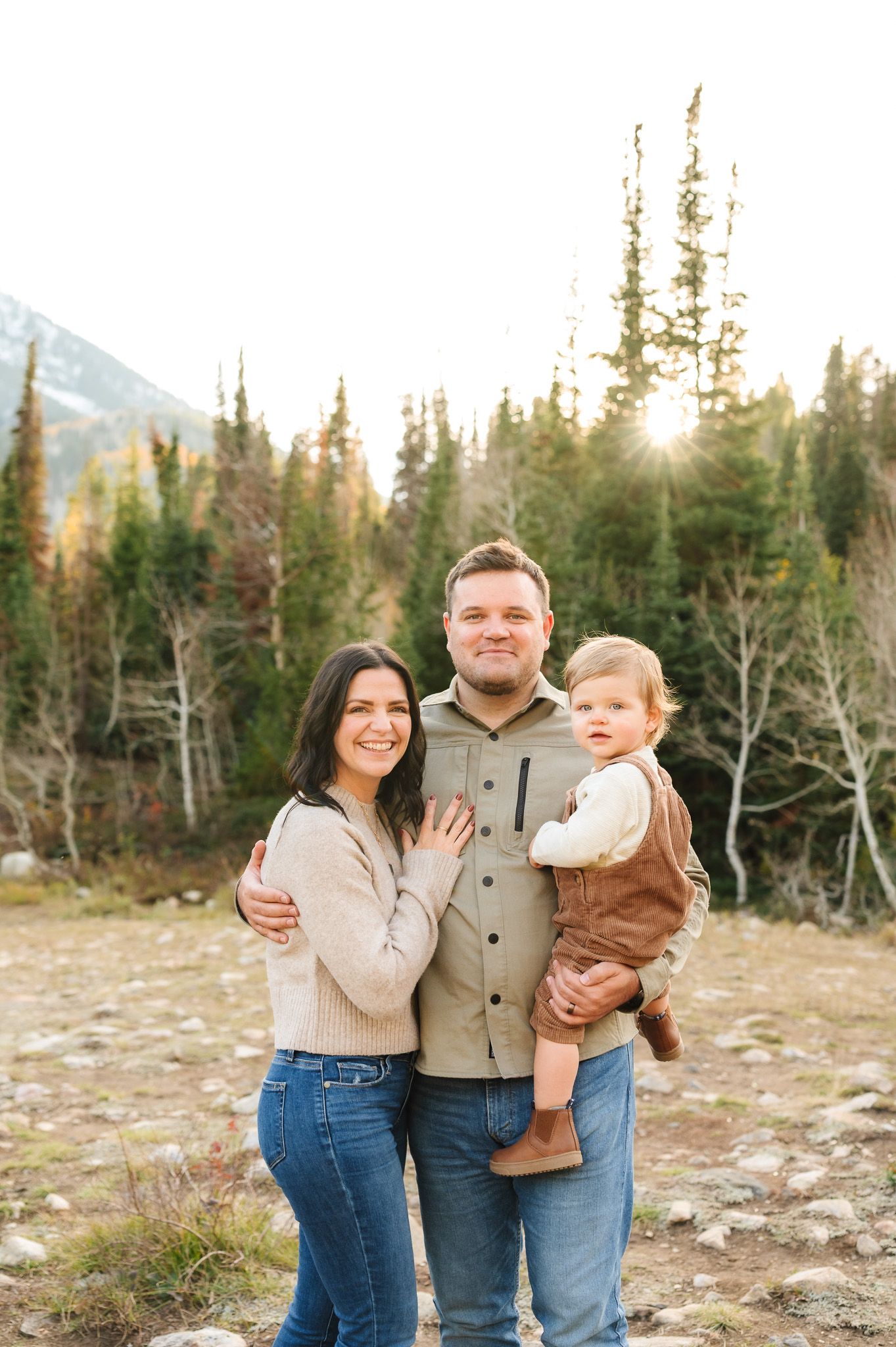 Family portrait in mountain setting with evergreen trees and sunlight.