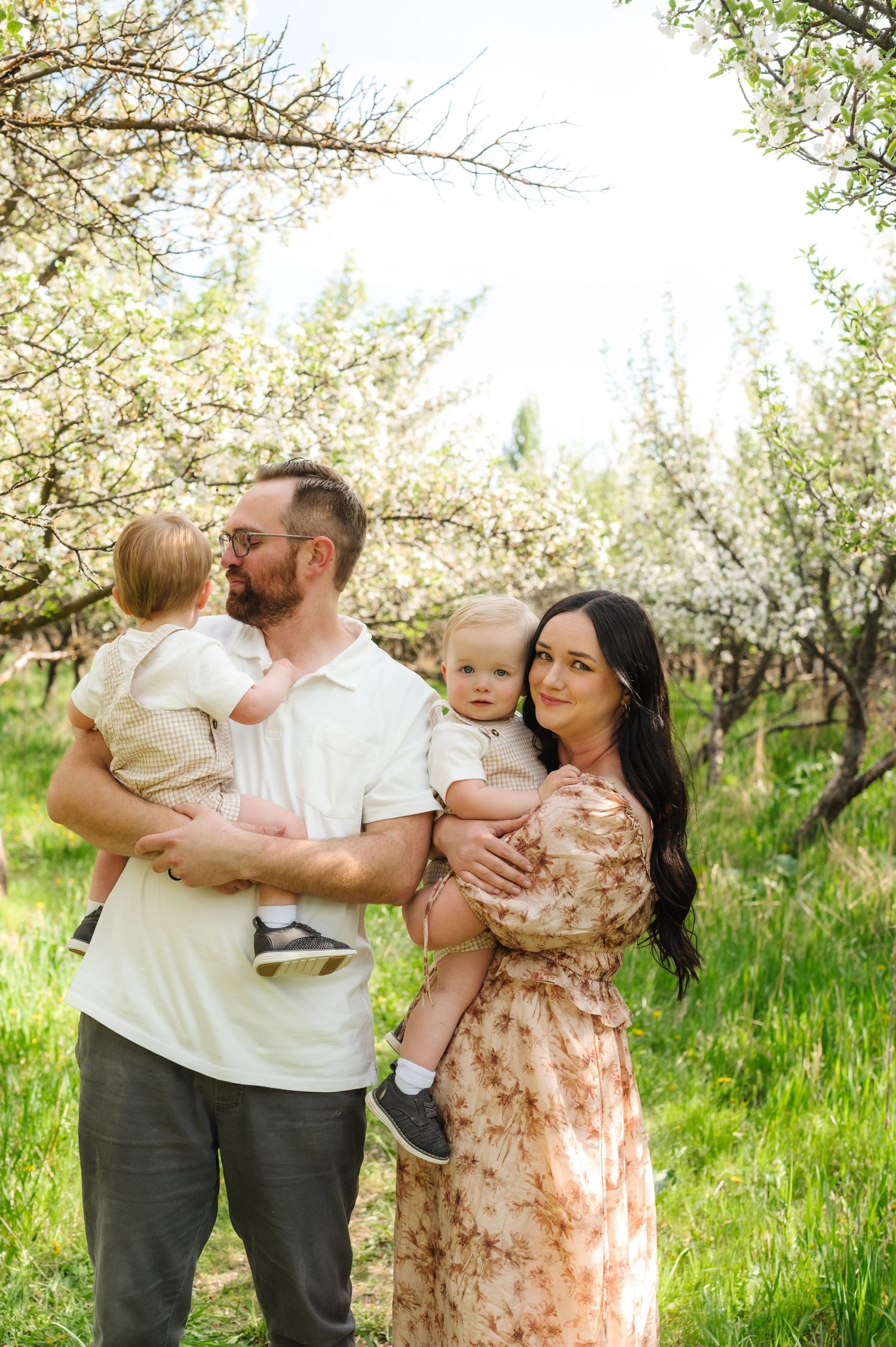 A family stands together in a blooming spring orchard with white blossoms and lush green grass in the background.