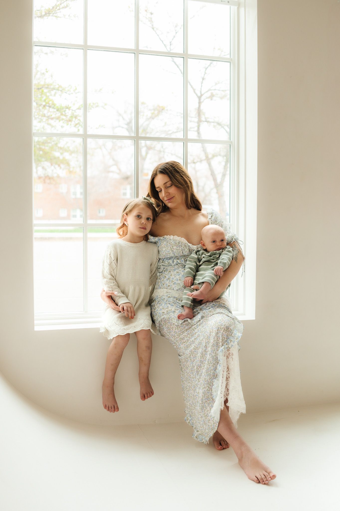 Family portrait featuring coordinating outfits in soft natural light by large window.