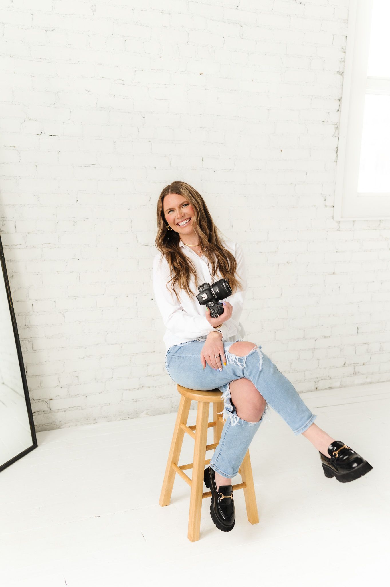 Casual studio portrait on wooden stool with camera and distressed denim style.