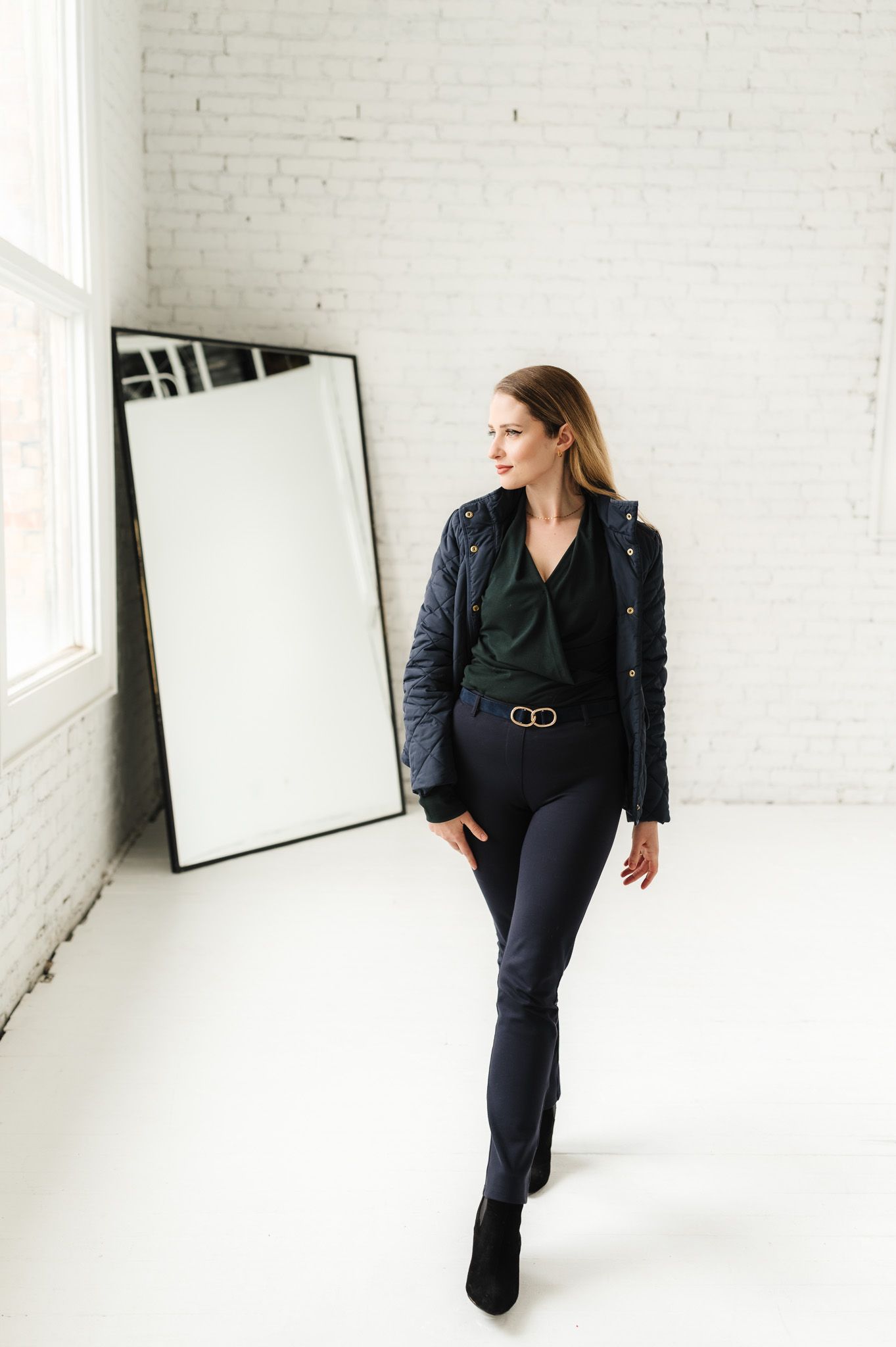 Stylish photographer in all black outfit and leather jacket poses in minimalist white studio.