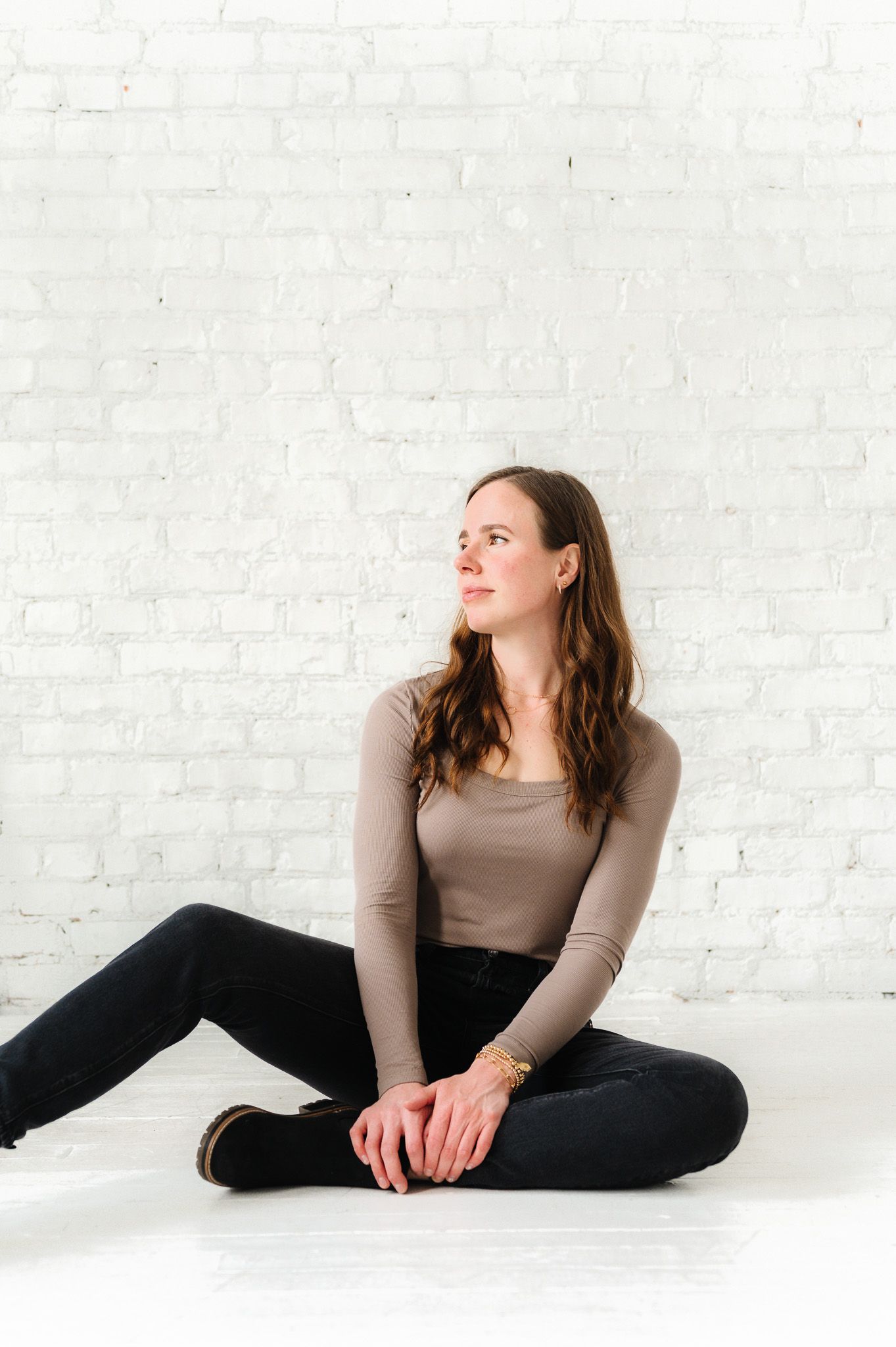 Casual portrait against white brick wall showing relaxed seated pose in studio setting.