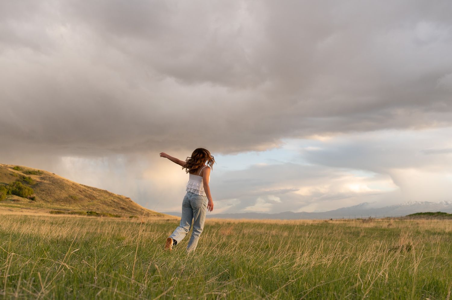 A young girl runs through a vast green meadow under dramatic storm clouds at golden hour.