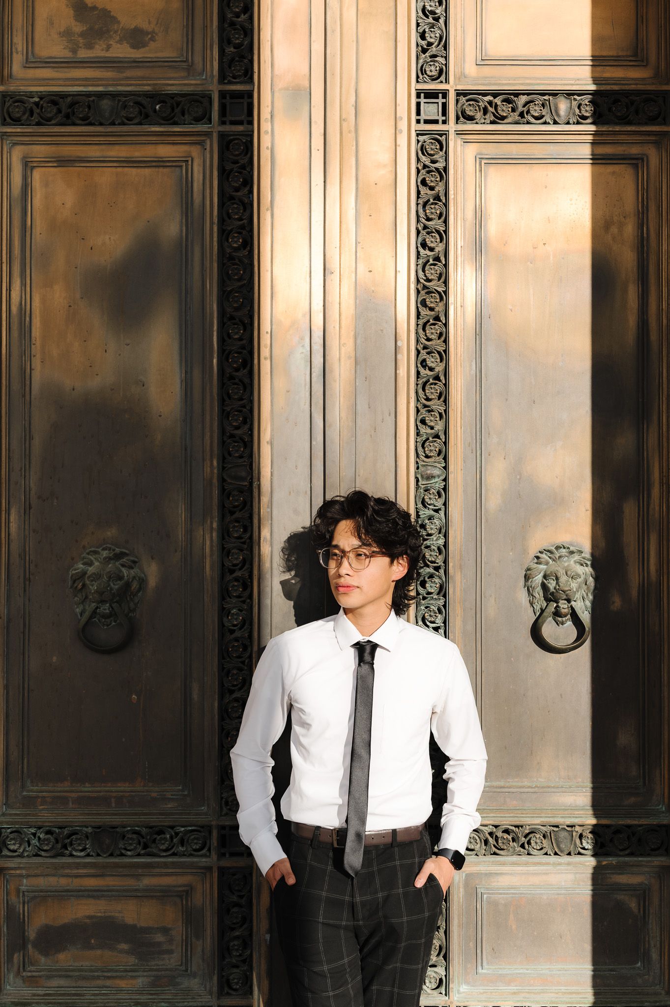 Person in formal attire poses against ornate dark wood paneled walls with decorative moldings.