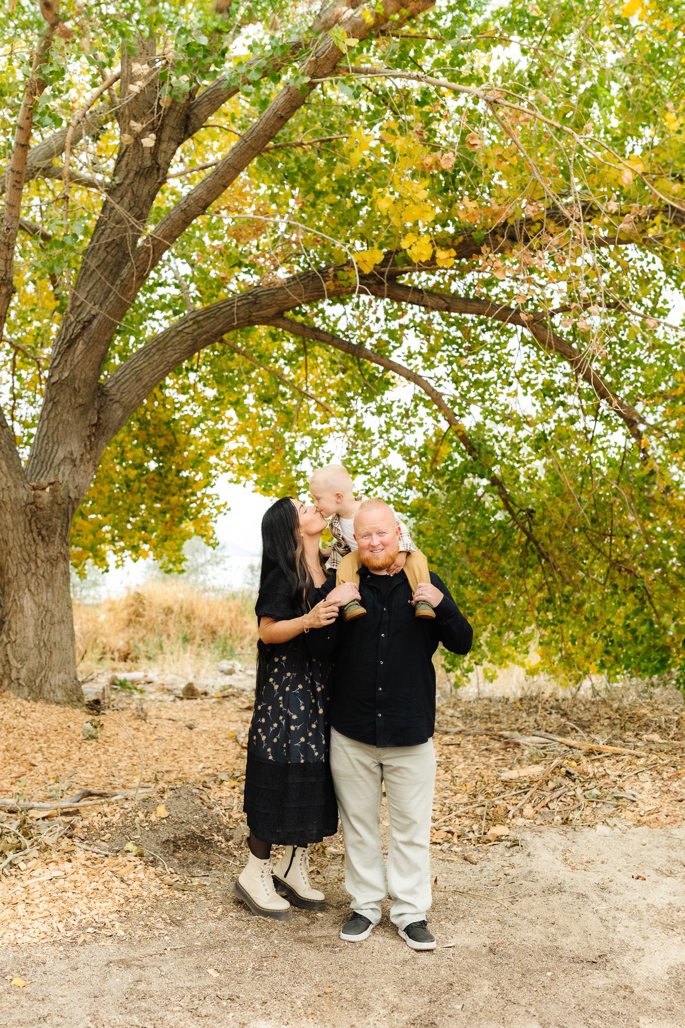Candid family photo session under trees with golden autumn leaves.