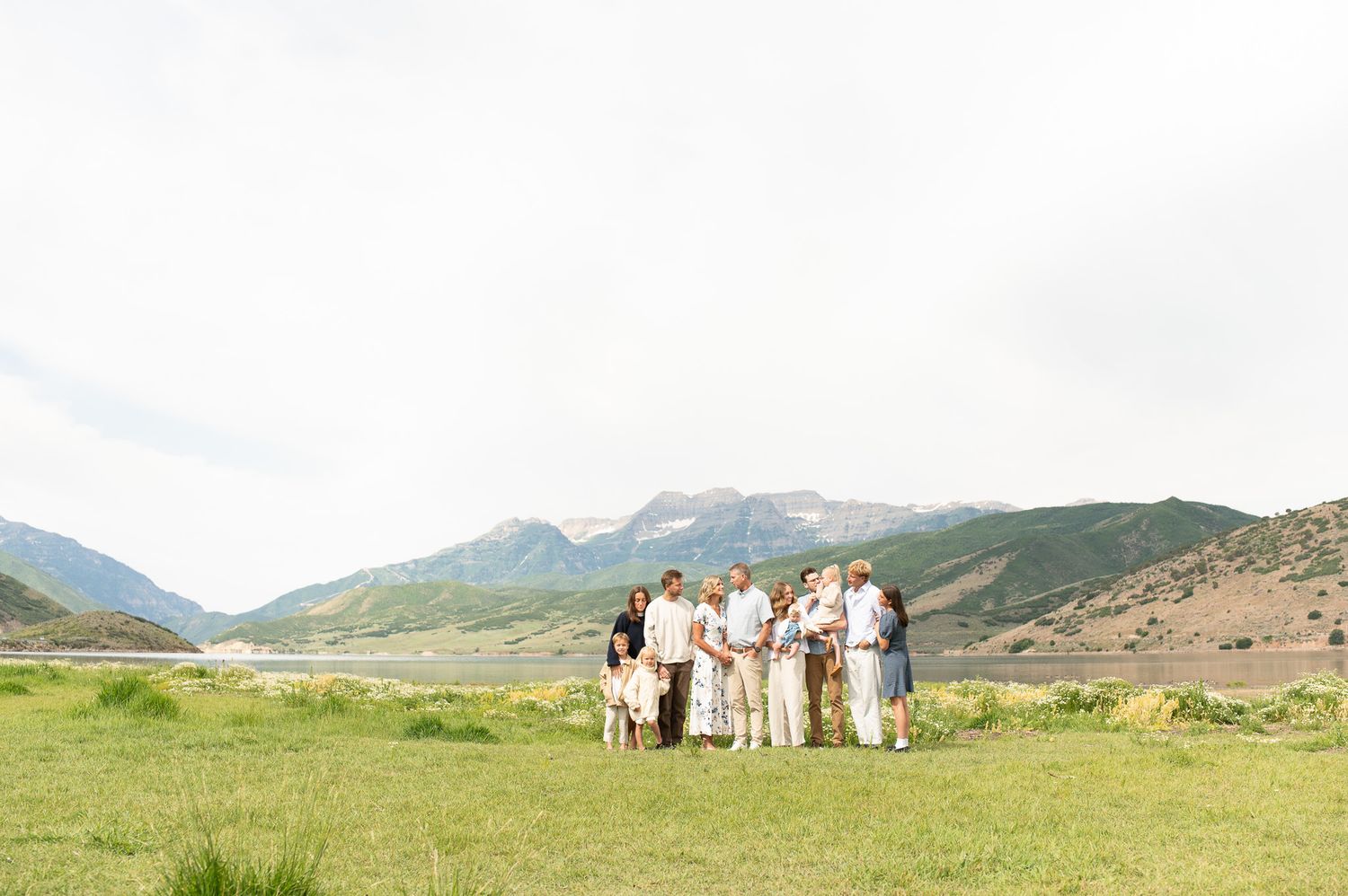Family group portrait in a green meadow with scenic mountain backdrop under a bright sky.