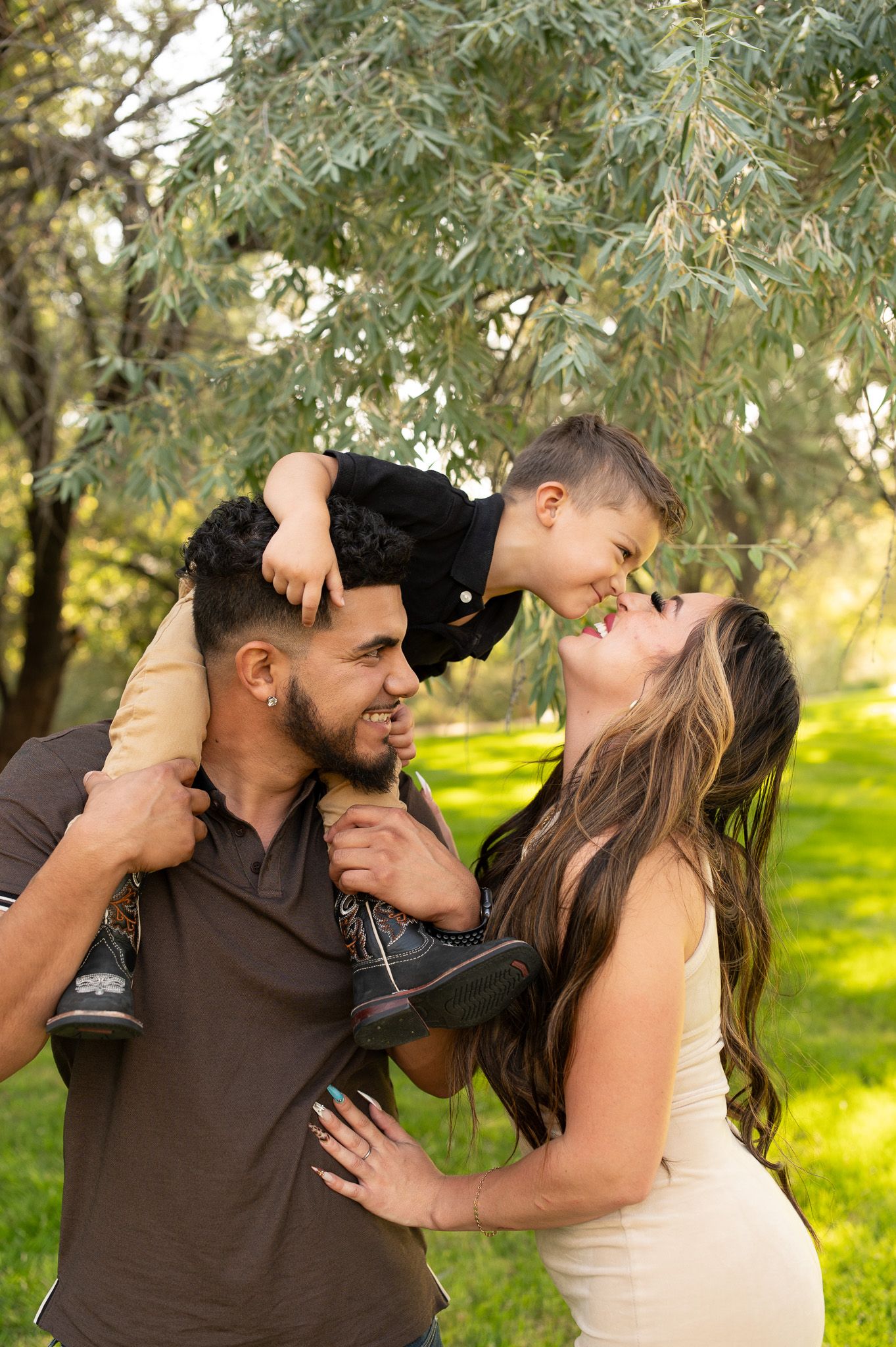 Happy young couple playing with toddler son lifted on shoulders in a sunny green park.