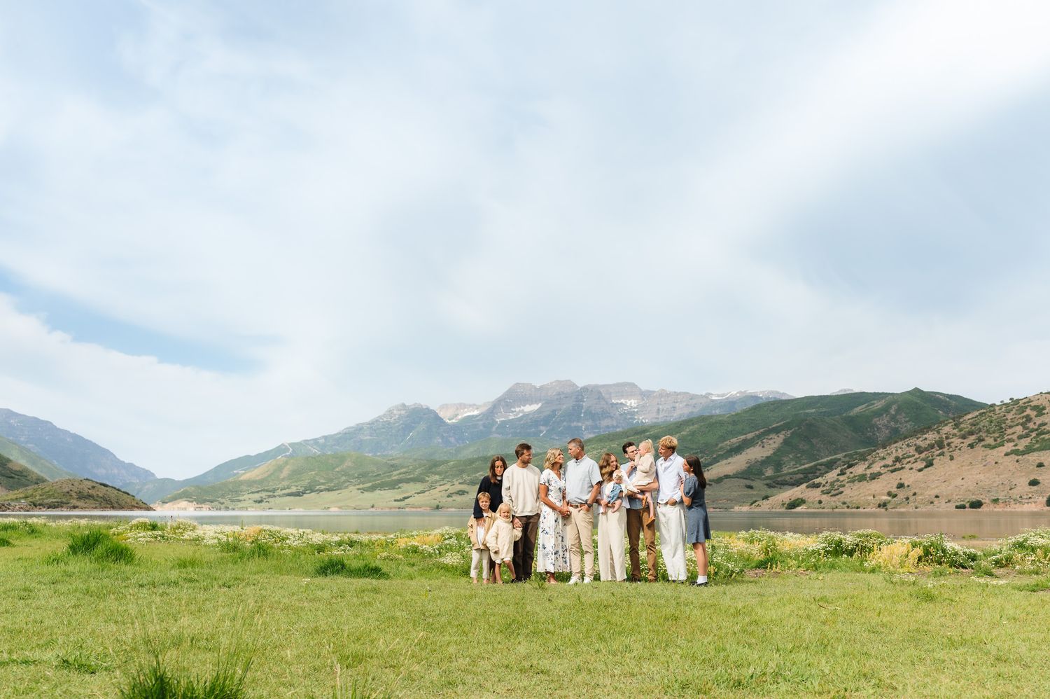 Group of people posing in a green meadow with scenic mountain backdrop under a partly cloudy sky.
