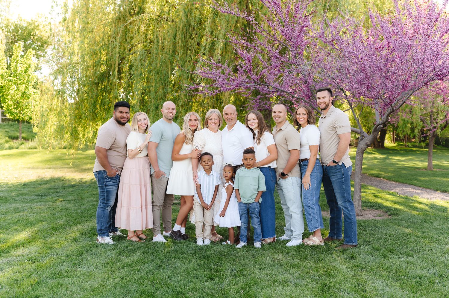 Extended family portrait taken in a scenic spring garden with blooming trees and green grass.