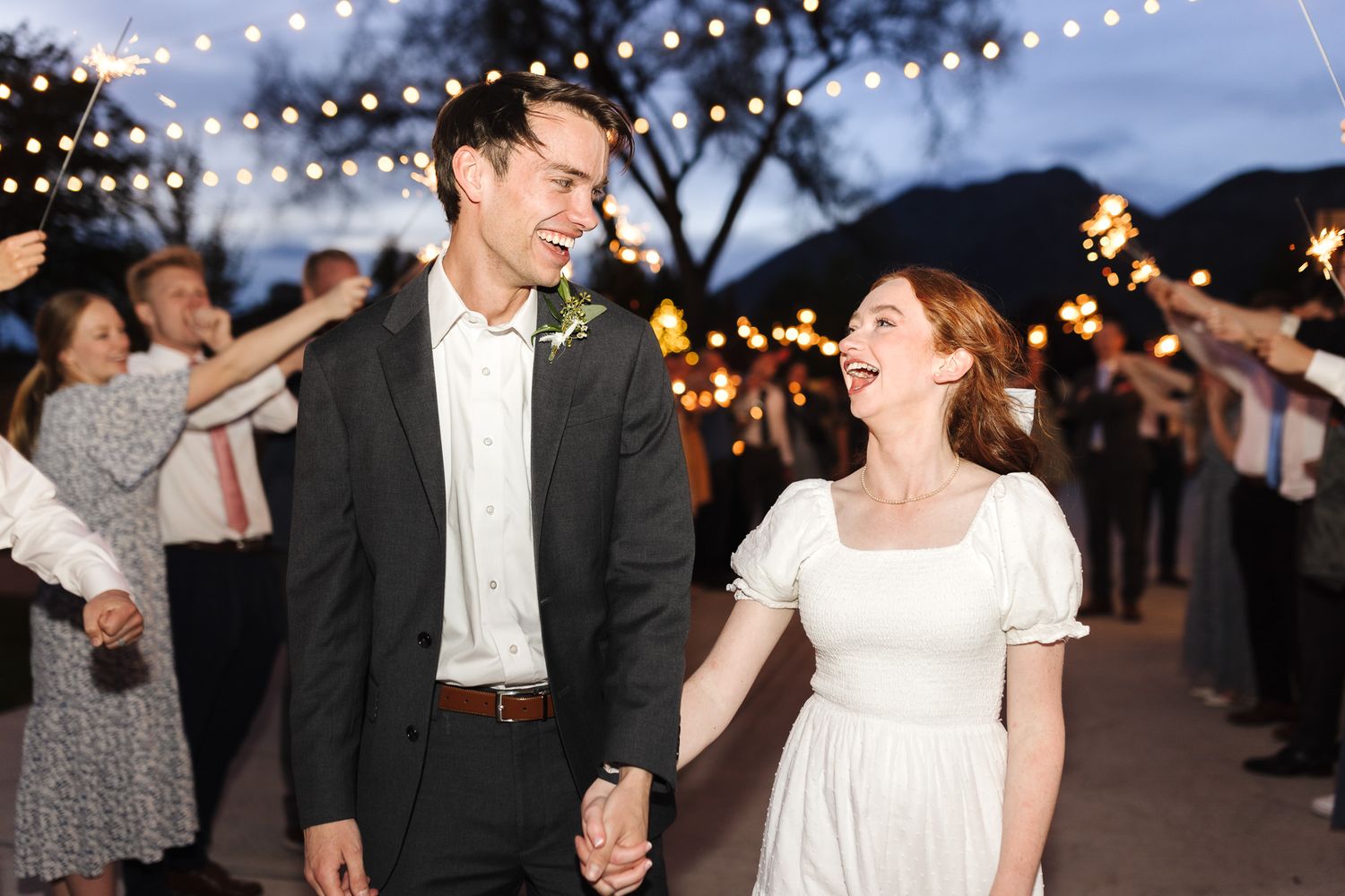 Joyful newlyweds walk hand-in-hand through a sparkler exit at their outdoor evening wedding reception.