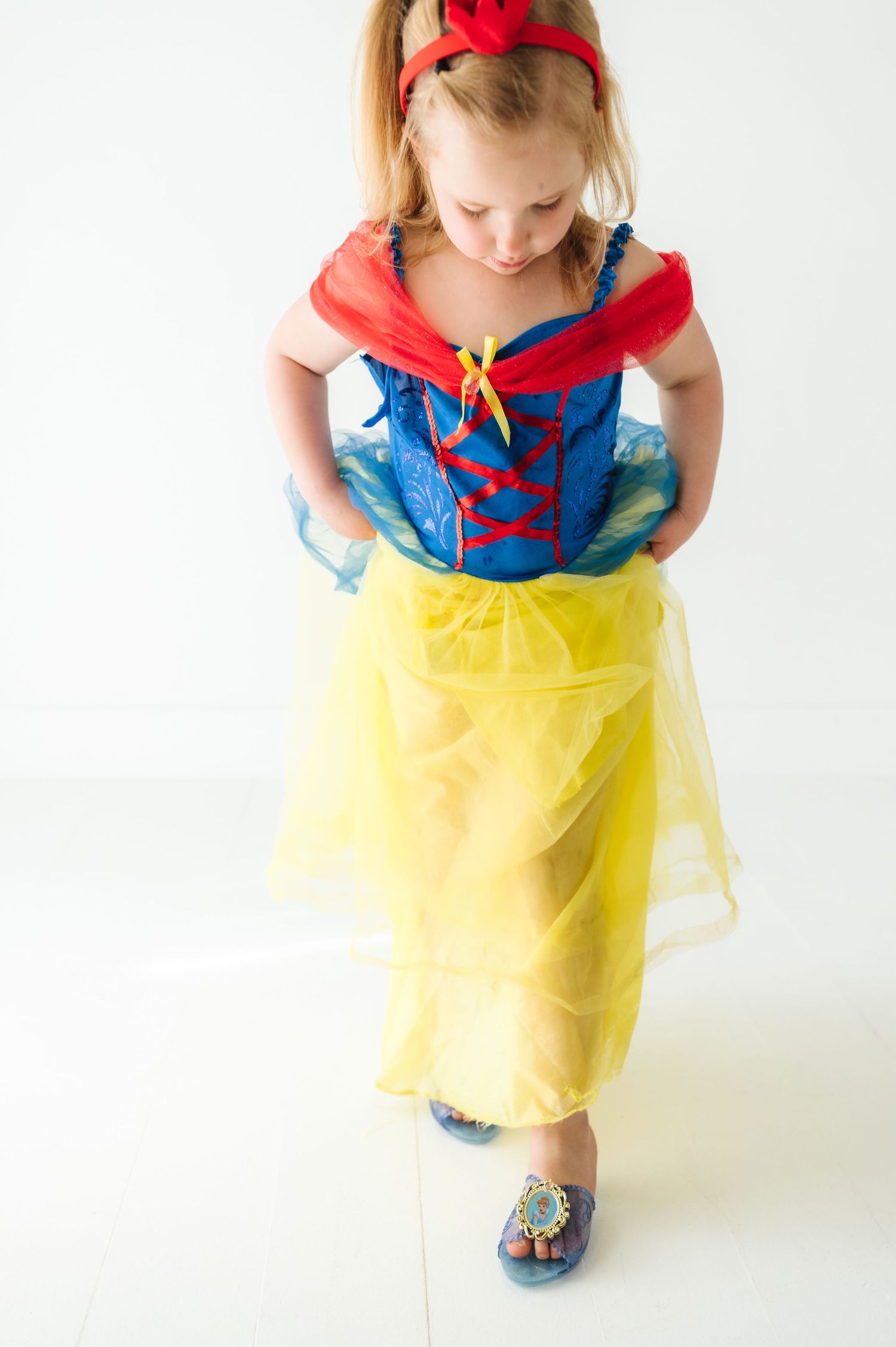 Young child wearing a Snow White inspired costume with red bow, blue top and yellow tulle skirt.