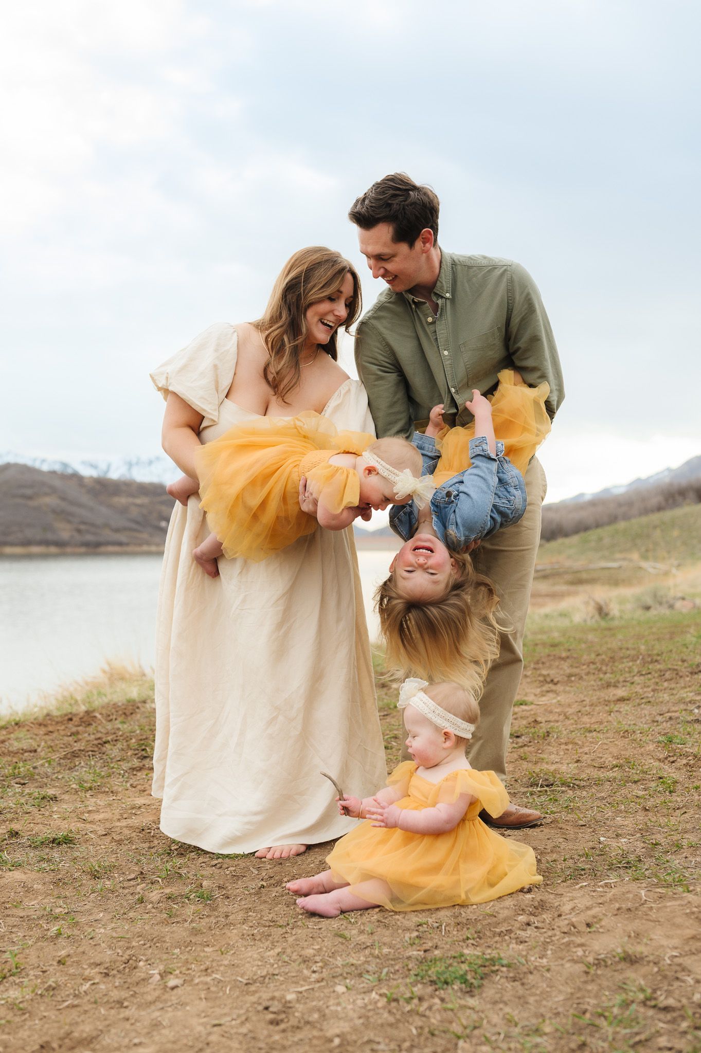 Family enjoying playful moments together on a scenic hillside in casual attire.