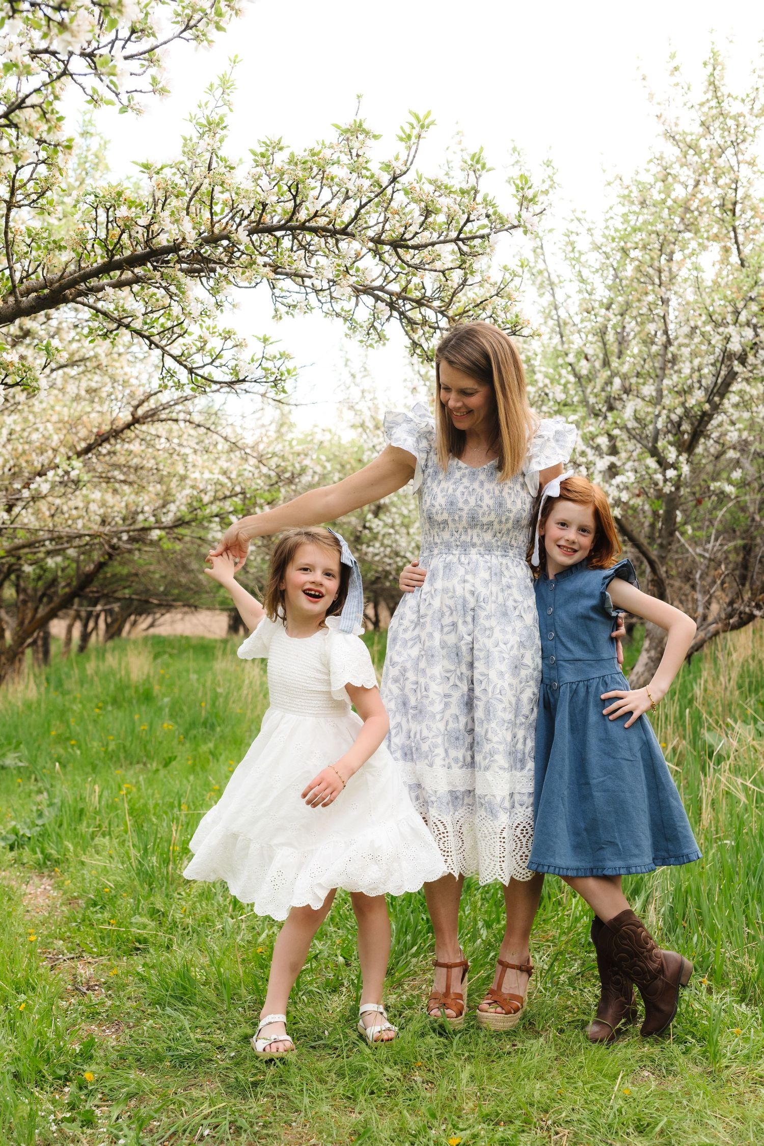 Children's feet wearing various shoes and boots stand together in a blooming spring orchard.