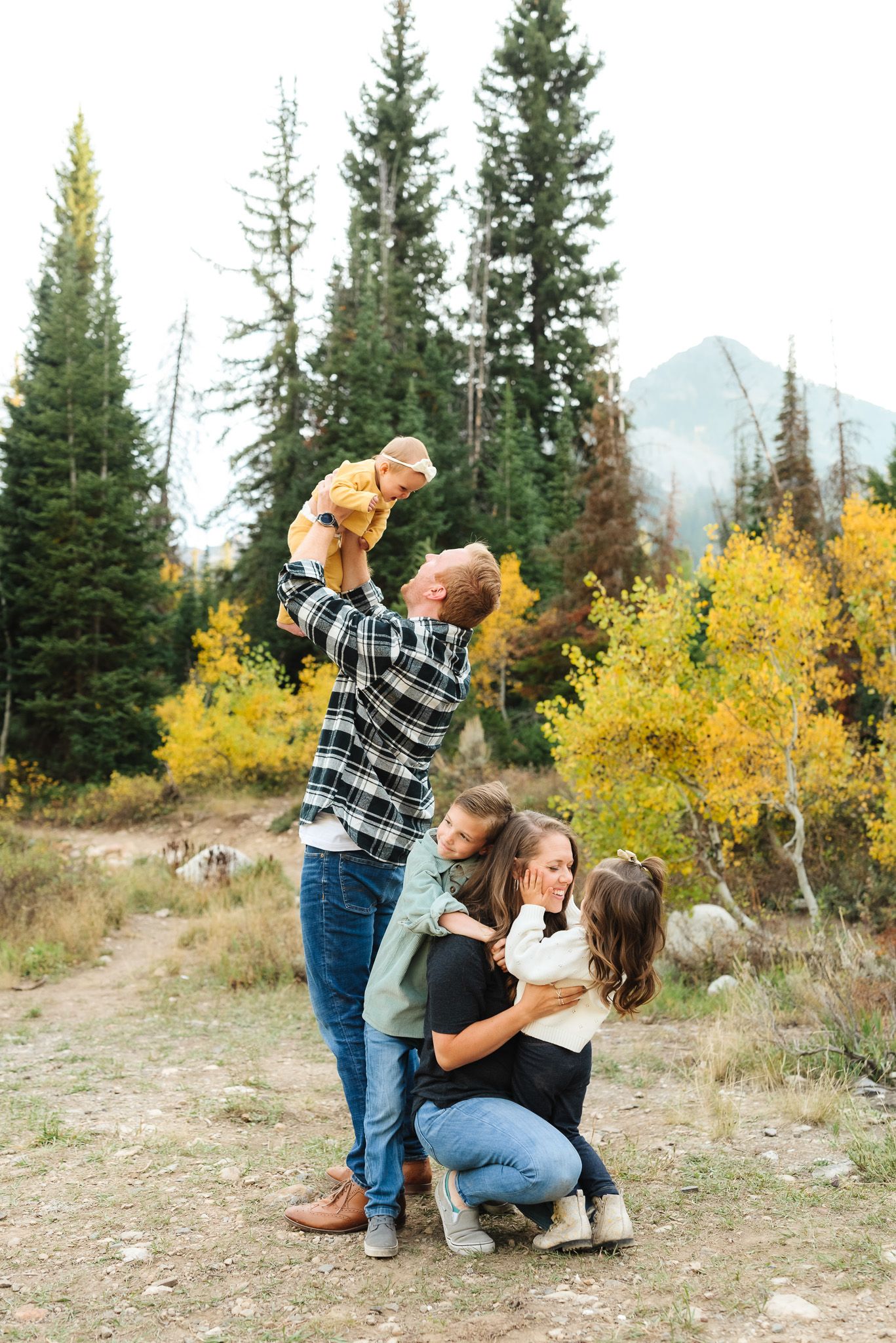 Child in mint green sweater posing playfully against autumn mountain backdrop.
