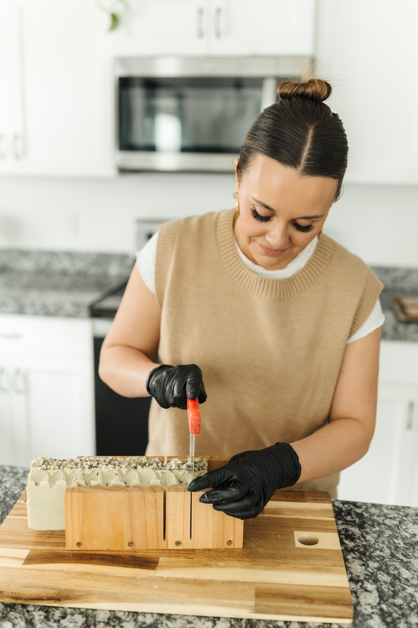 Someone wearing black gloves prepares food on a wooden cutting board in a bright modern kitchen.