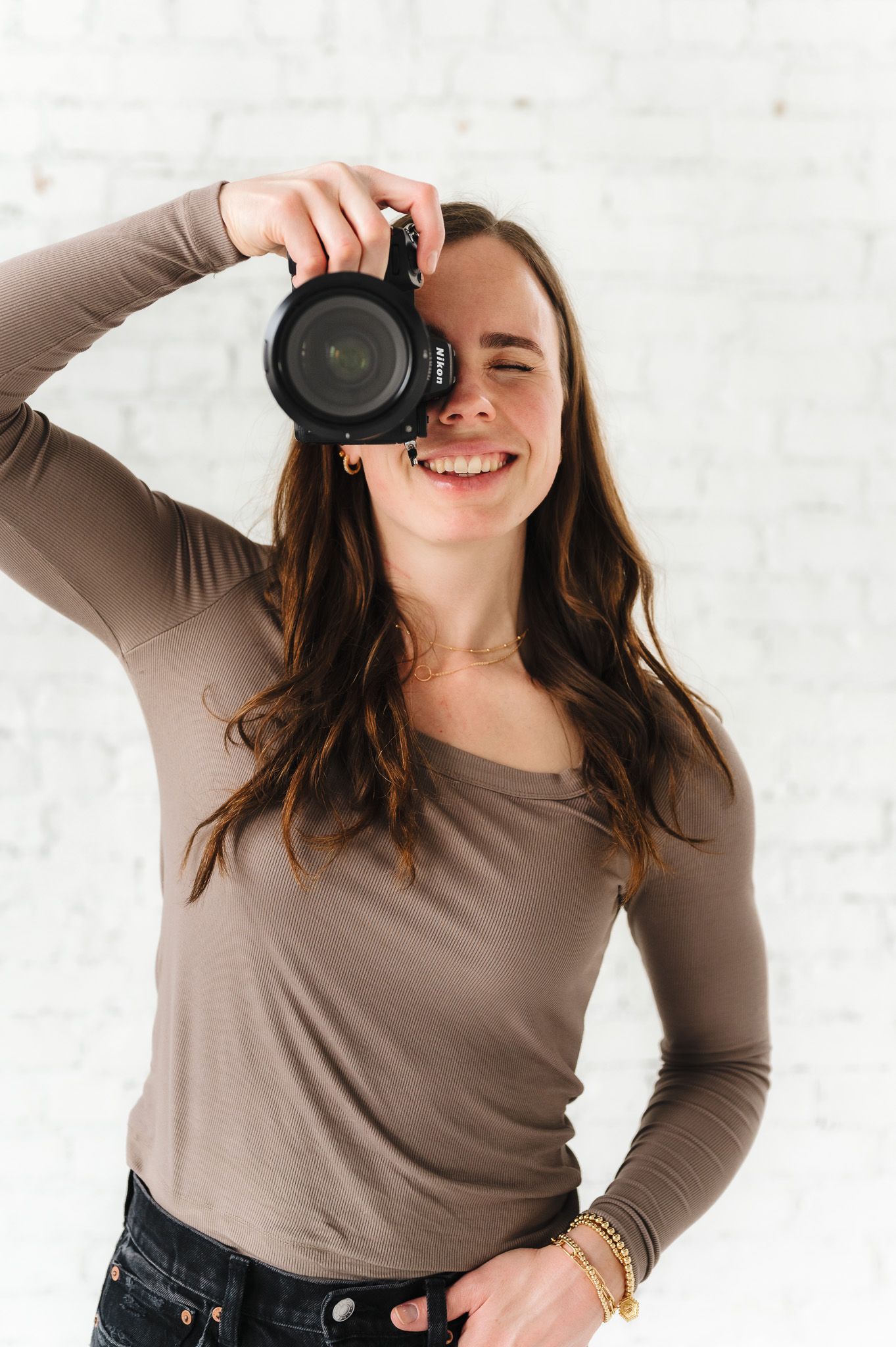 Photographer takes picture with DSLR camera while smiling in studio.