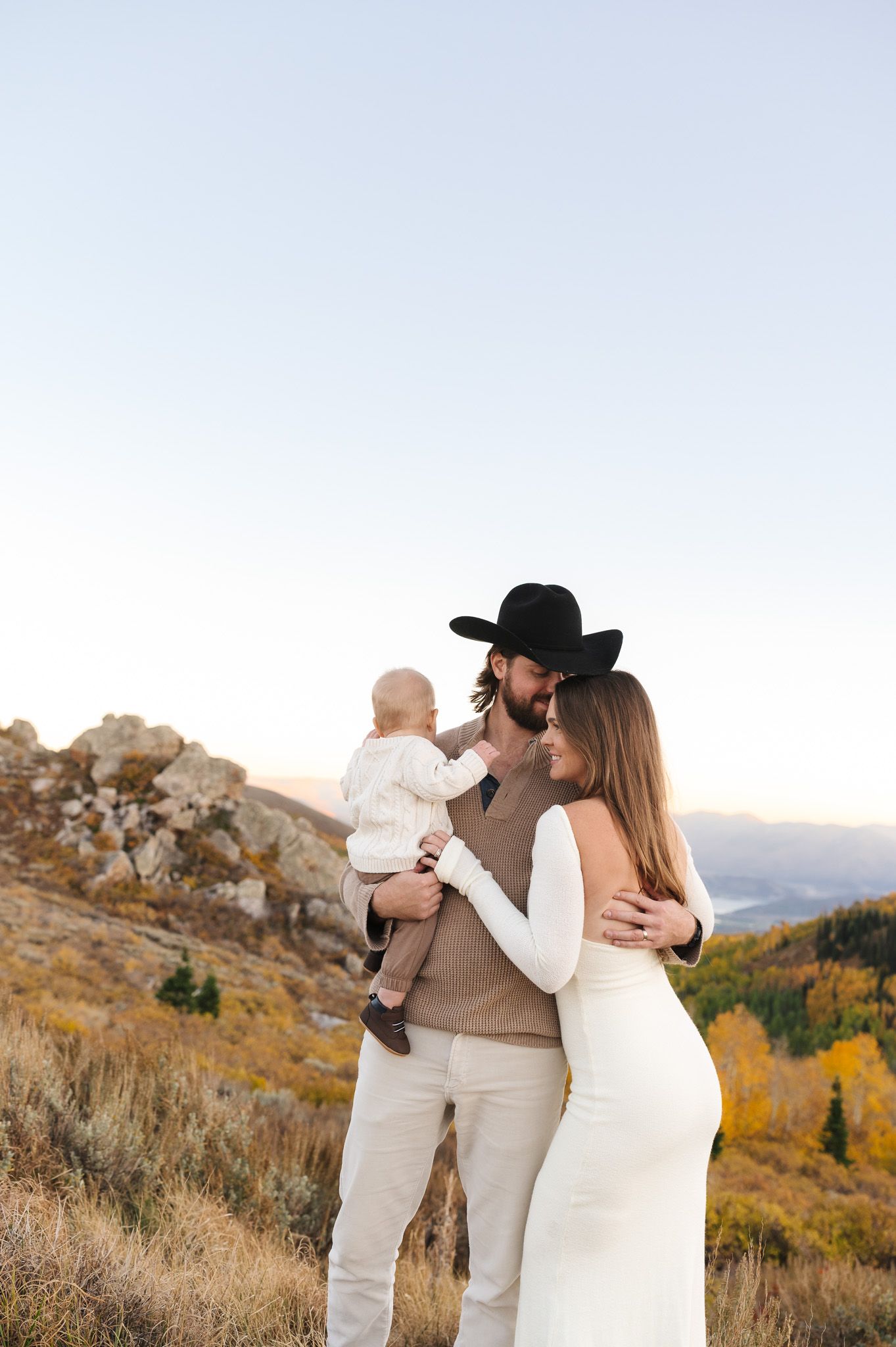 A couple shares a romantic moment on a mountain ridge during sunset wearing coordinated neutral outfits.