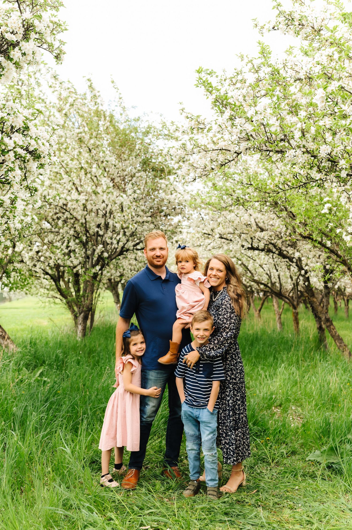 Family portrait session in a blooming spring orchard with white blossoms.