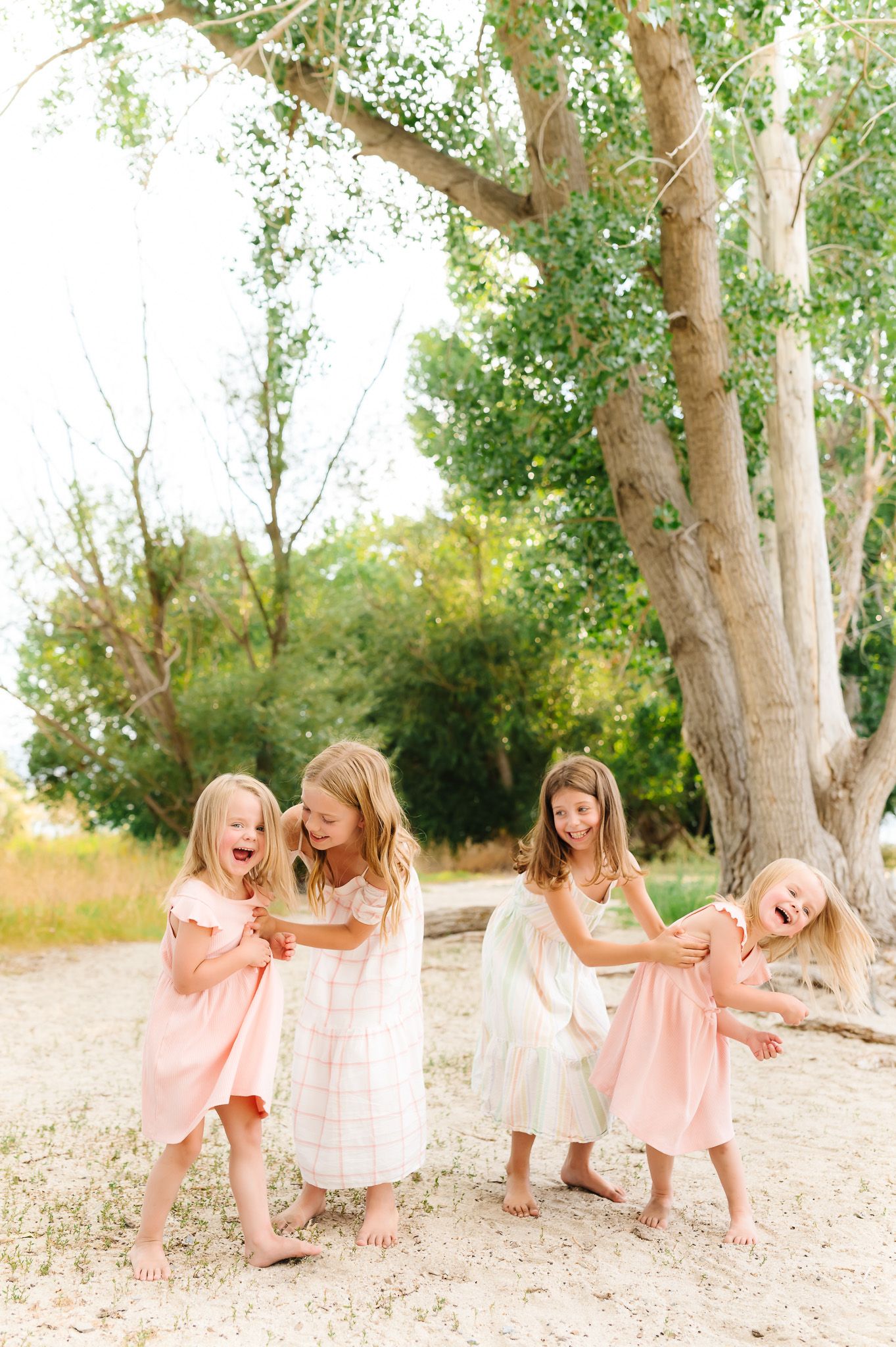 Two young girls in pink dresses play and dance together in a sunlit wooded area.