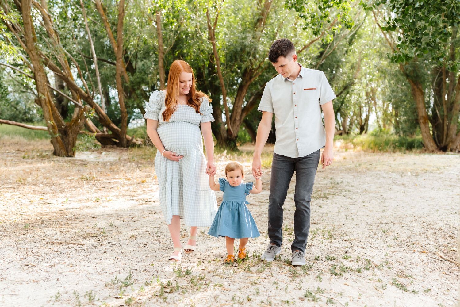 Family walking together through a sunlit wooded area during a summer photo session.