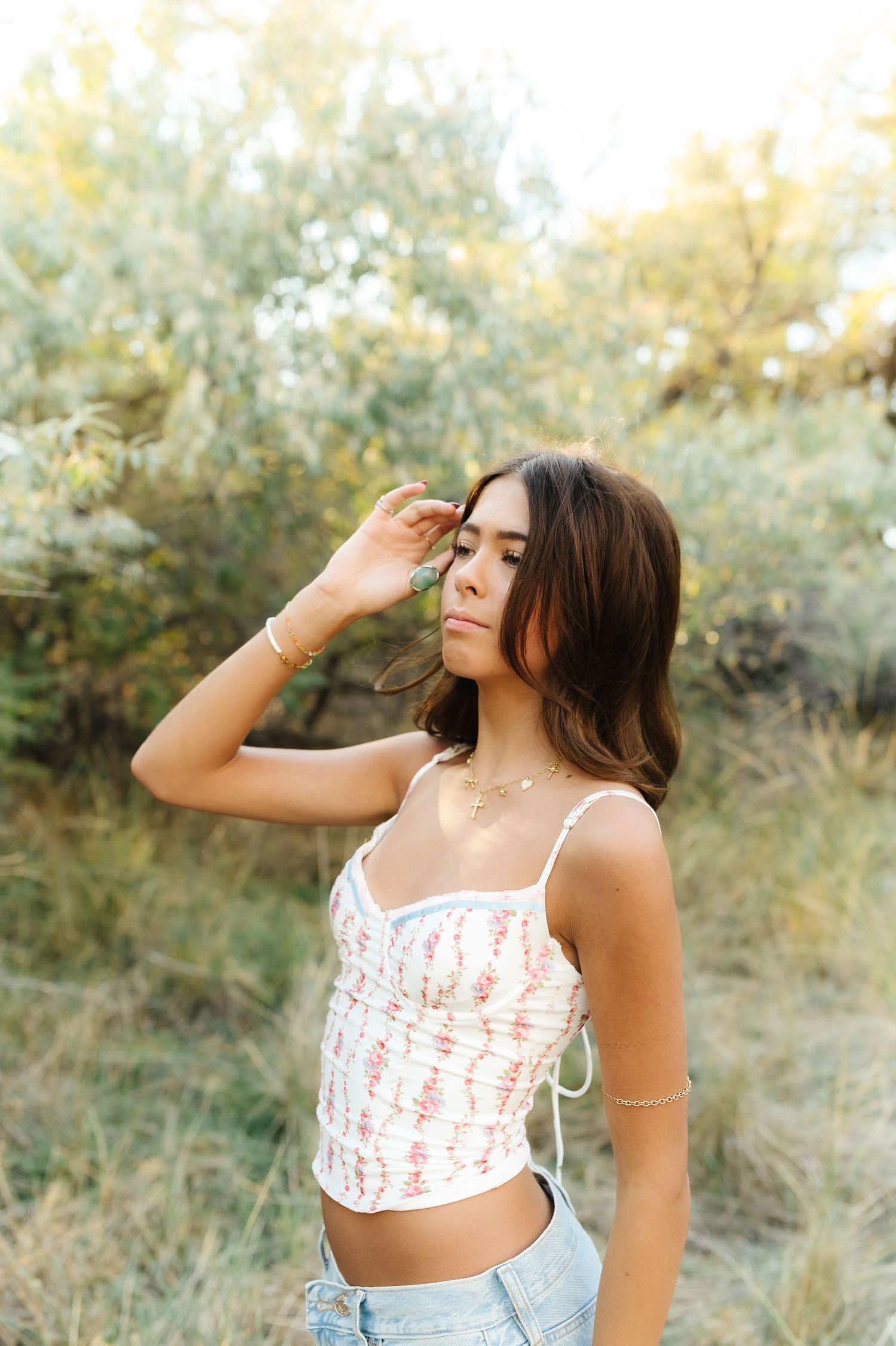 Woman in floral crop top poses in natural outdoor setting with dreamy lighting.