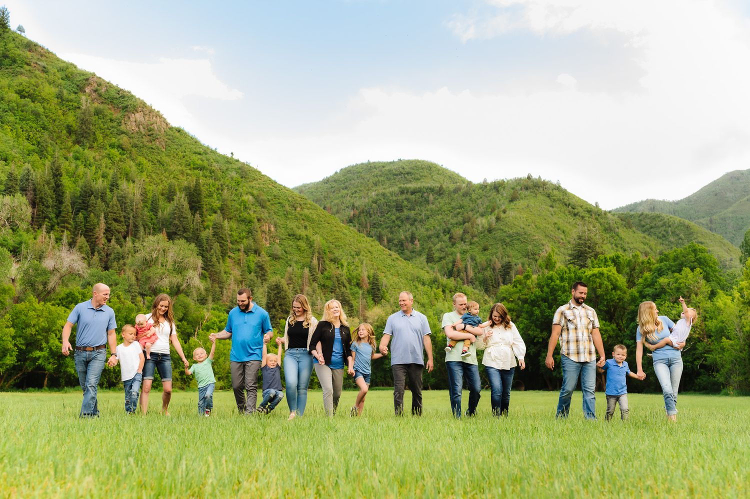 Group of people walking together across a green meadow with mountains in the background.