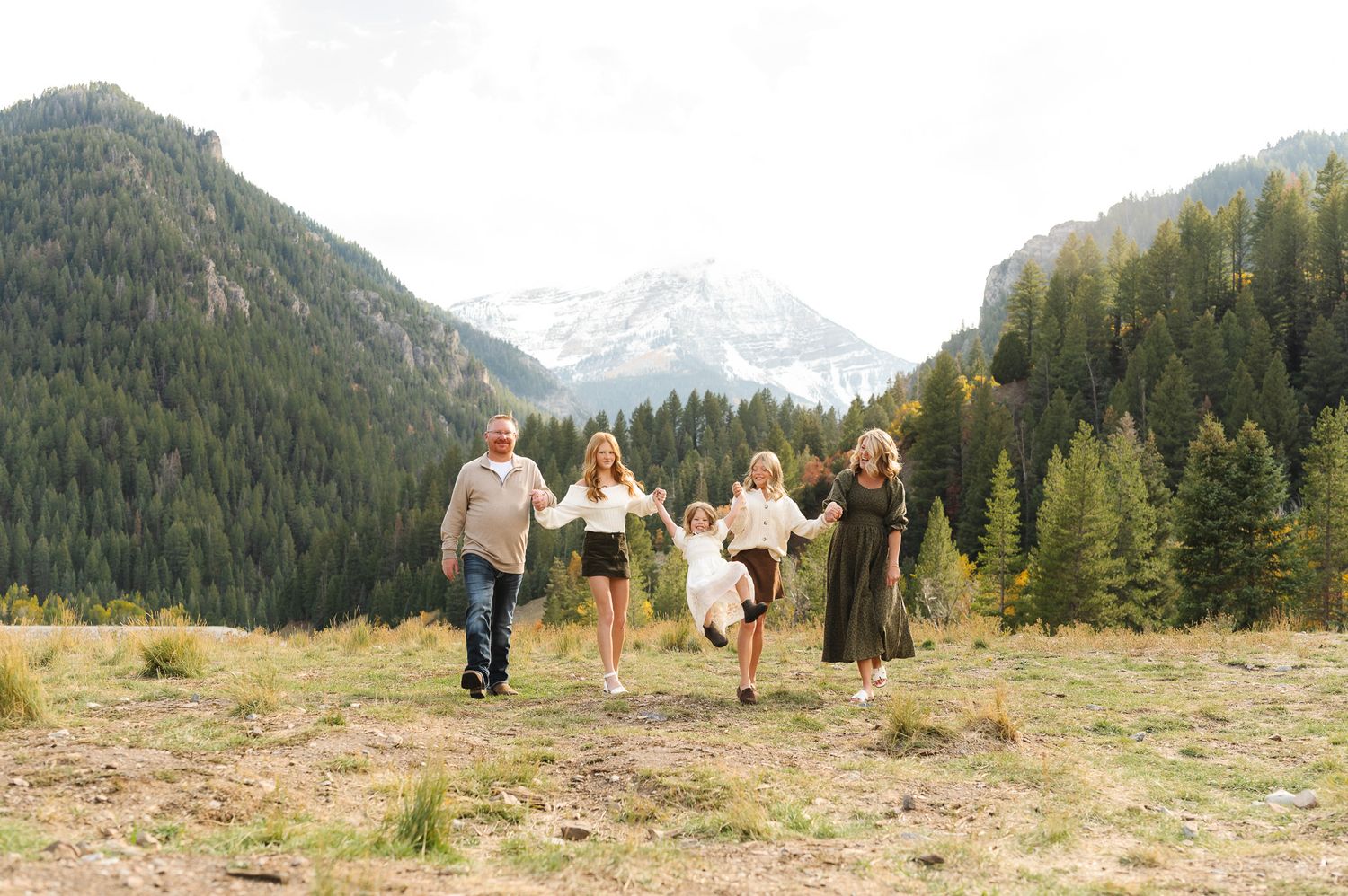 A group of people walking along a mountain trail with evergreen forests and snow-capped peaks in getting family photos at Tibble Fork.