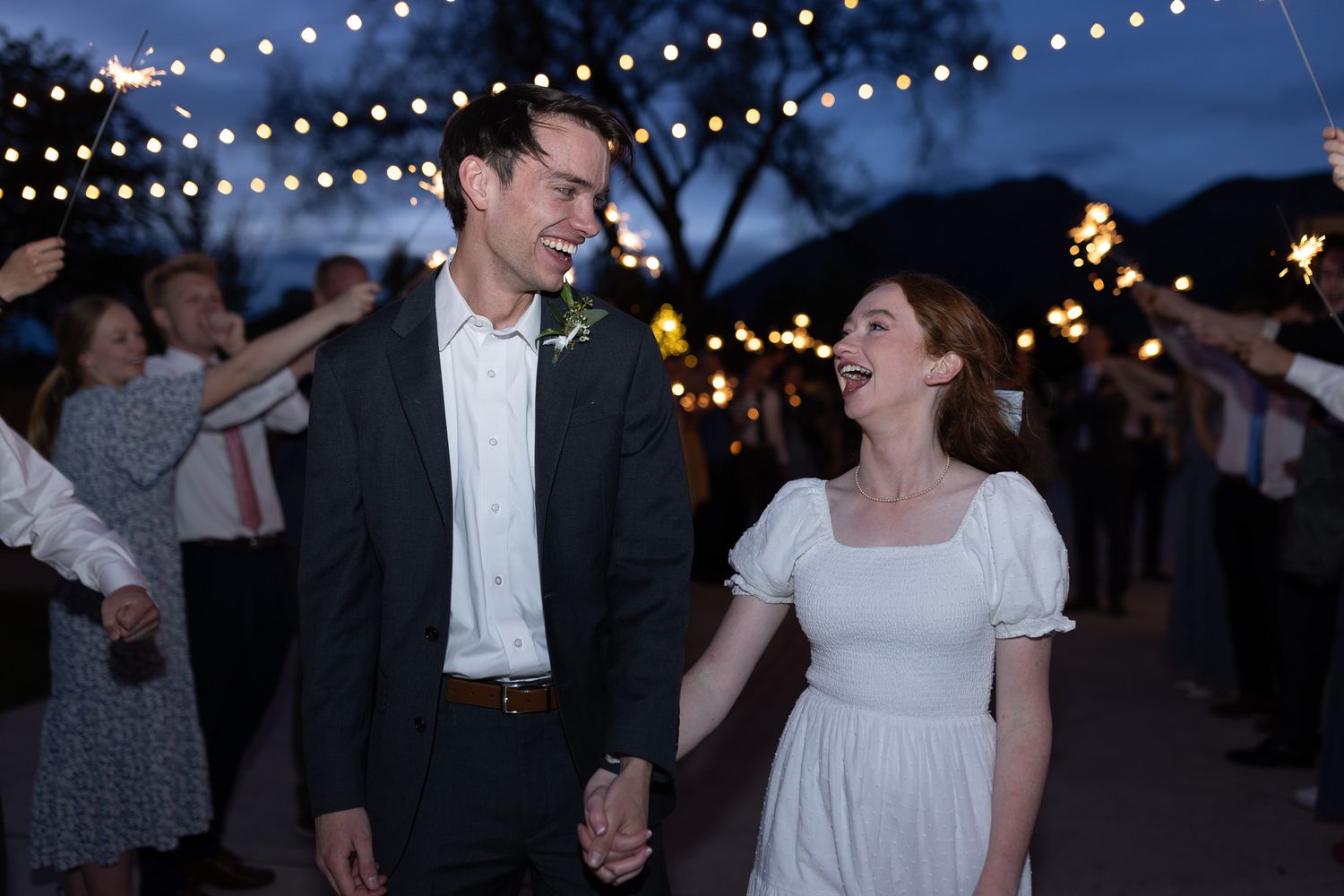 A joyful bride and groom hold hands during a sparkler send-off at their outdoor evening wedding reception.