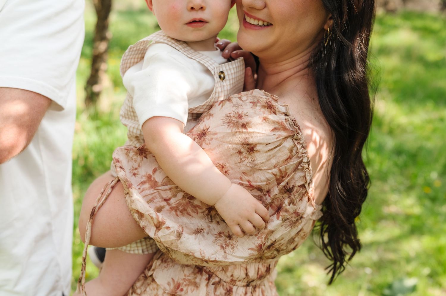 A toddler in a flowing pink dress plays in a grassy outdoor setting during a sunny day.