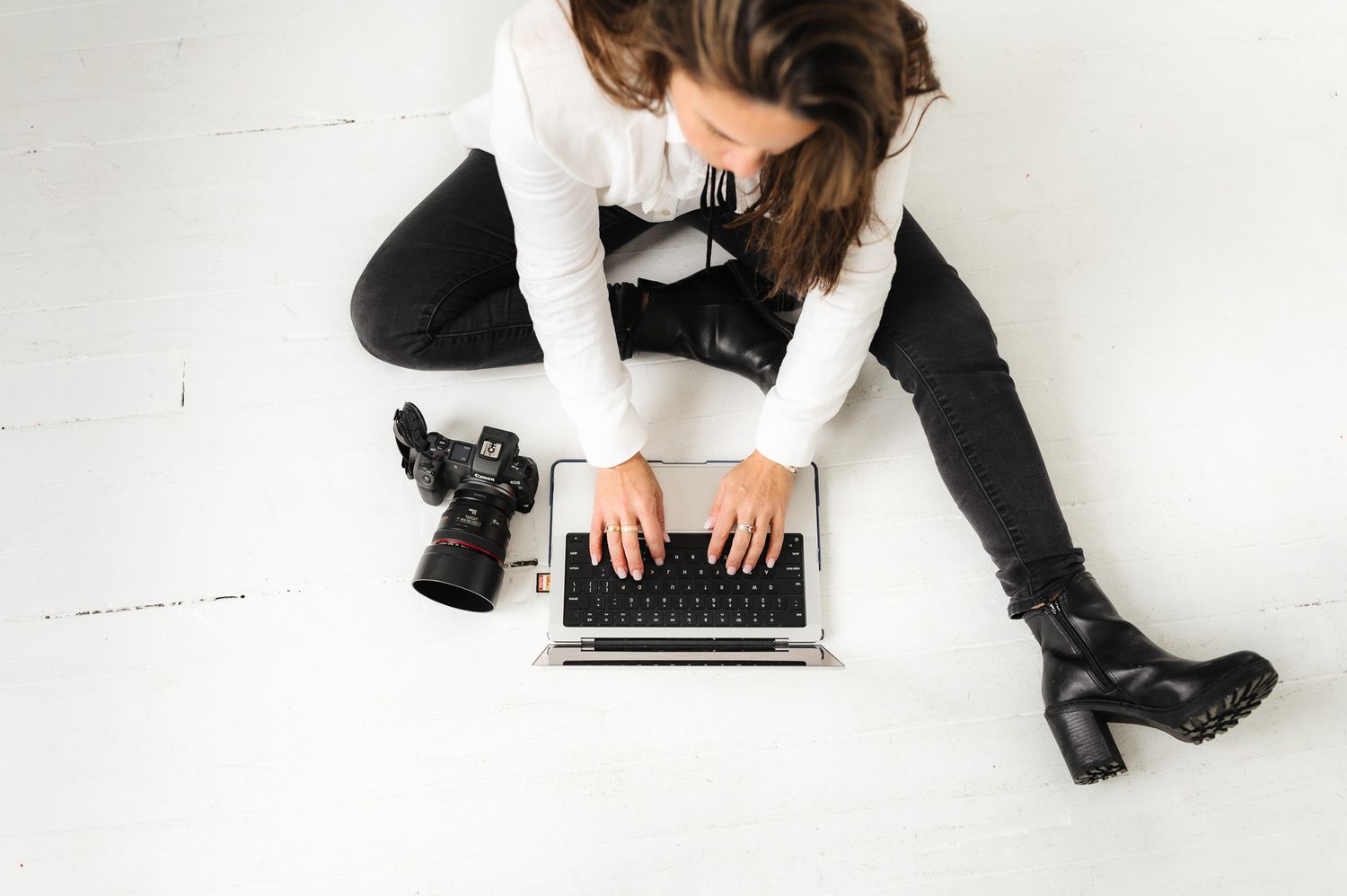 Overhead view of person working on laptop with camera beside them on white floor.