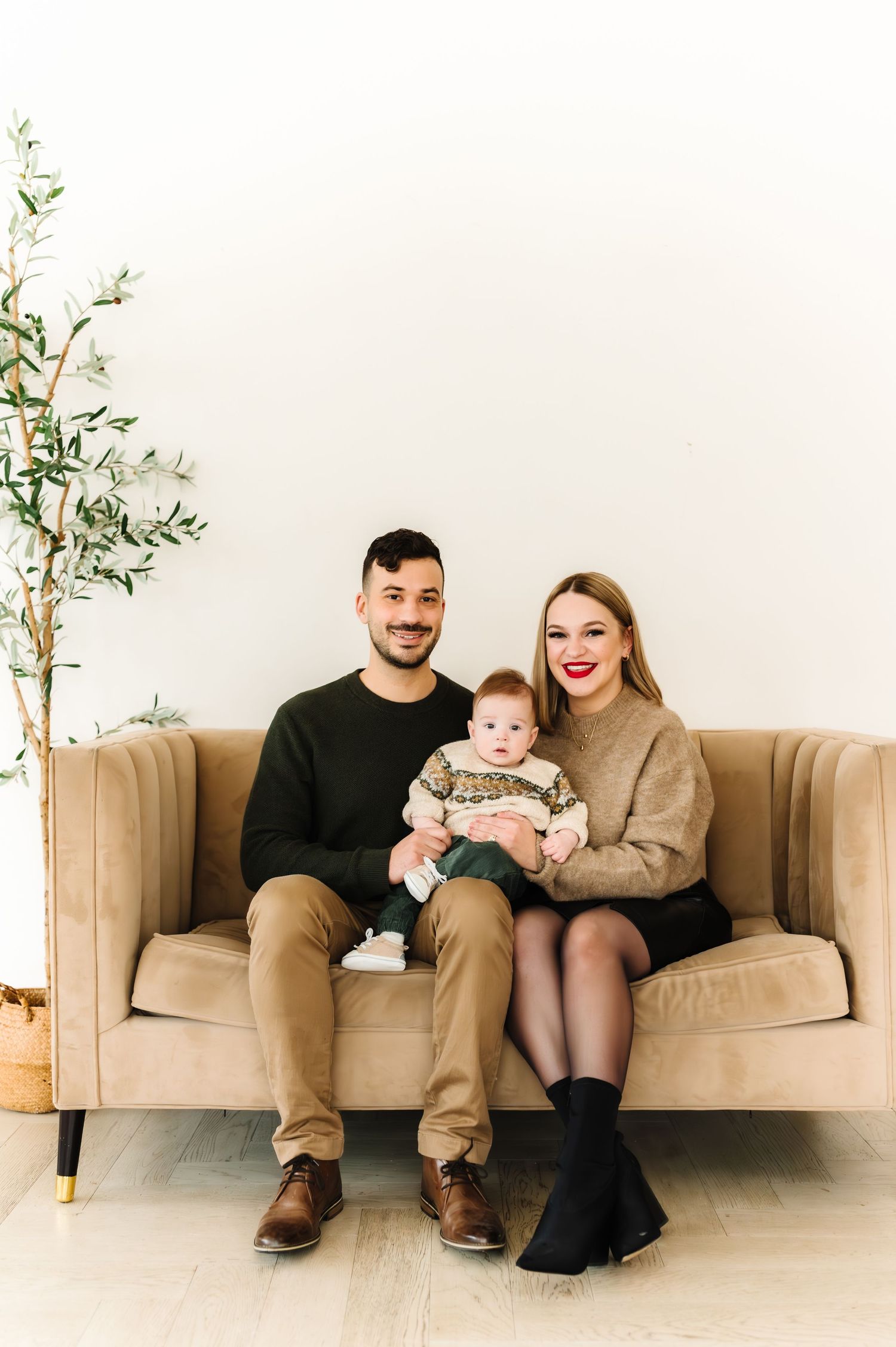 Family sits together on a beige couch in a minimalist room with potted plants.