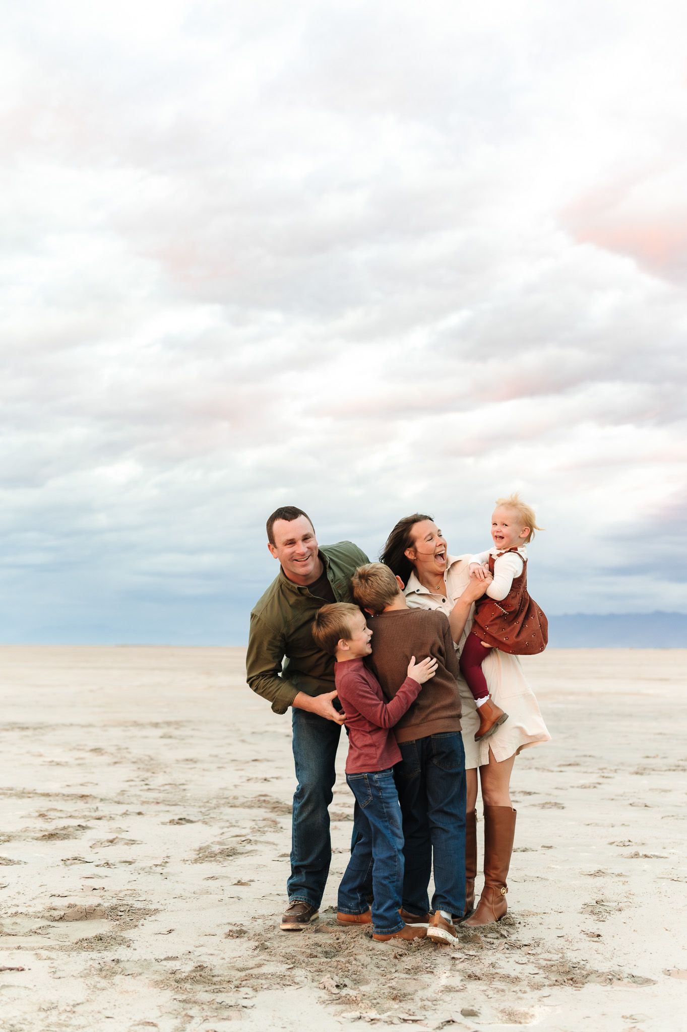 Happy family of five laughing together on a sandy beach under a dramatic cloudy sky.