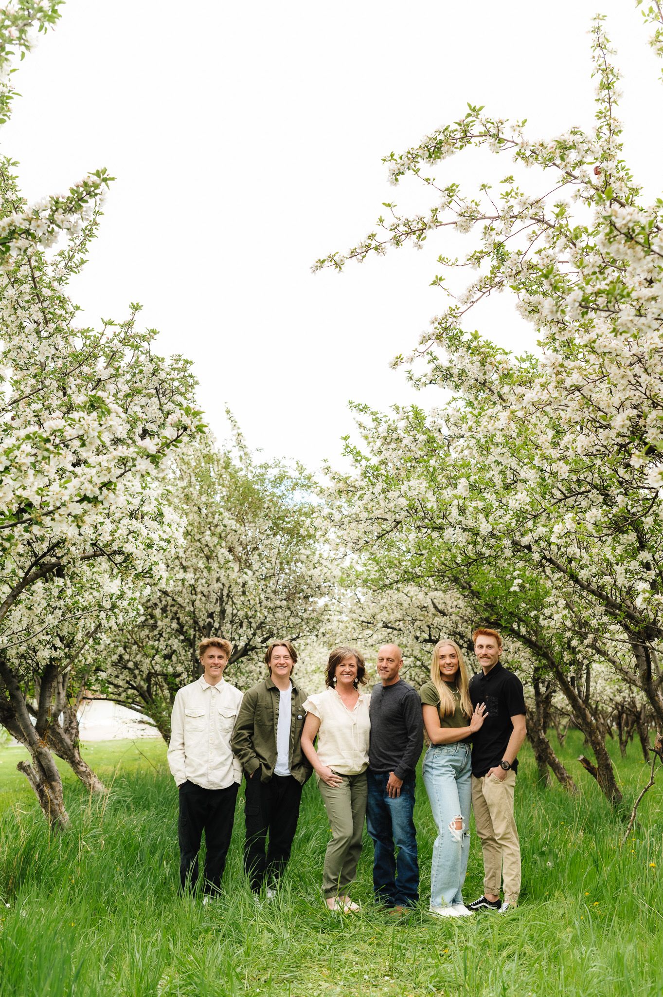 A group poses together under blooming white cherry trees in a grassy spring orchard.