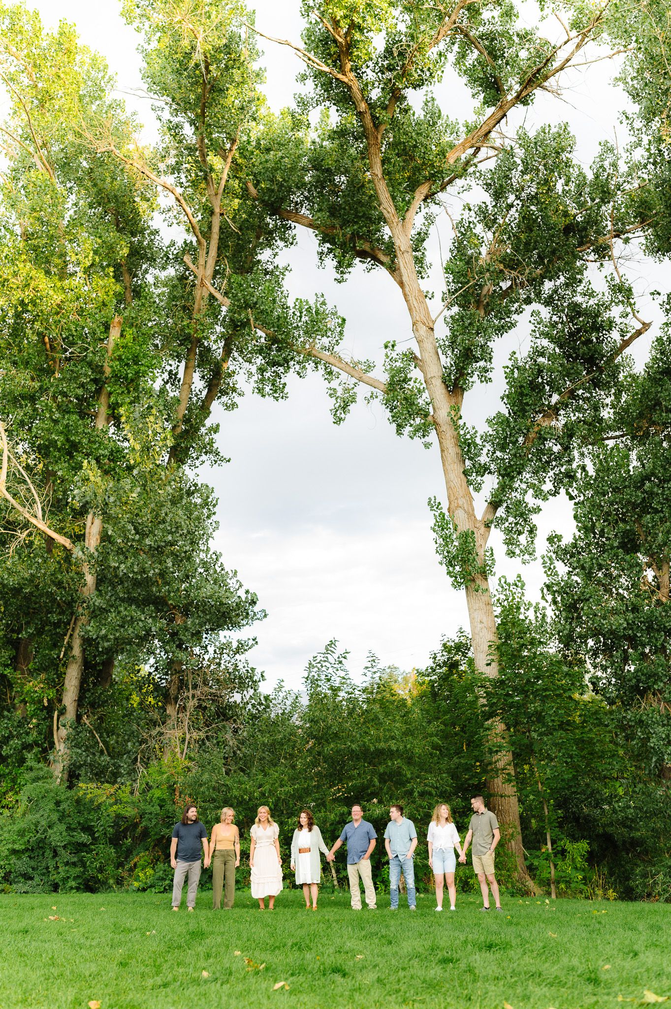 People standing in a line against tall green poplar trees on a grassy hillside.