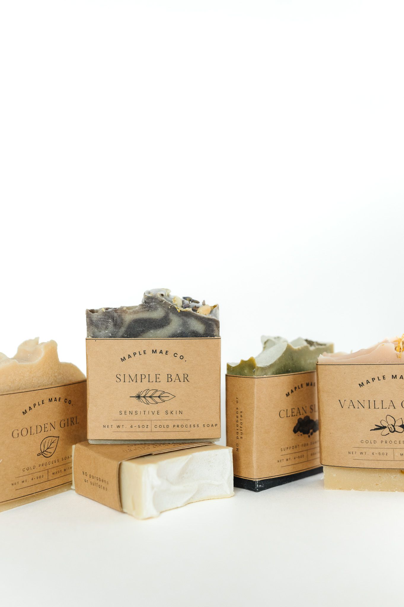 A row of Simple Raw soap boxes in neutral beige tones displaying various scents and product packaging designs.