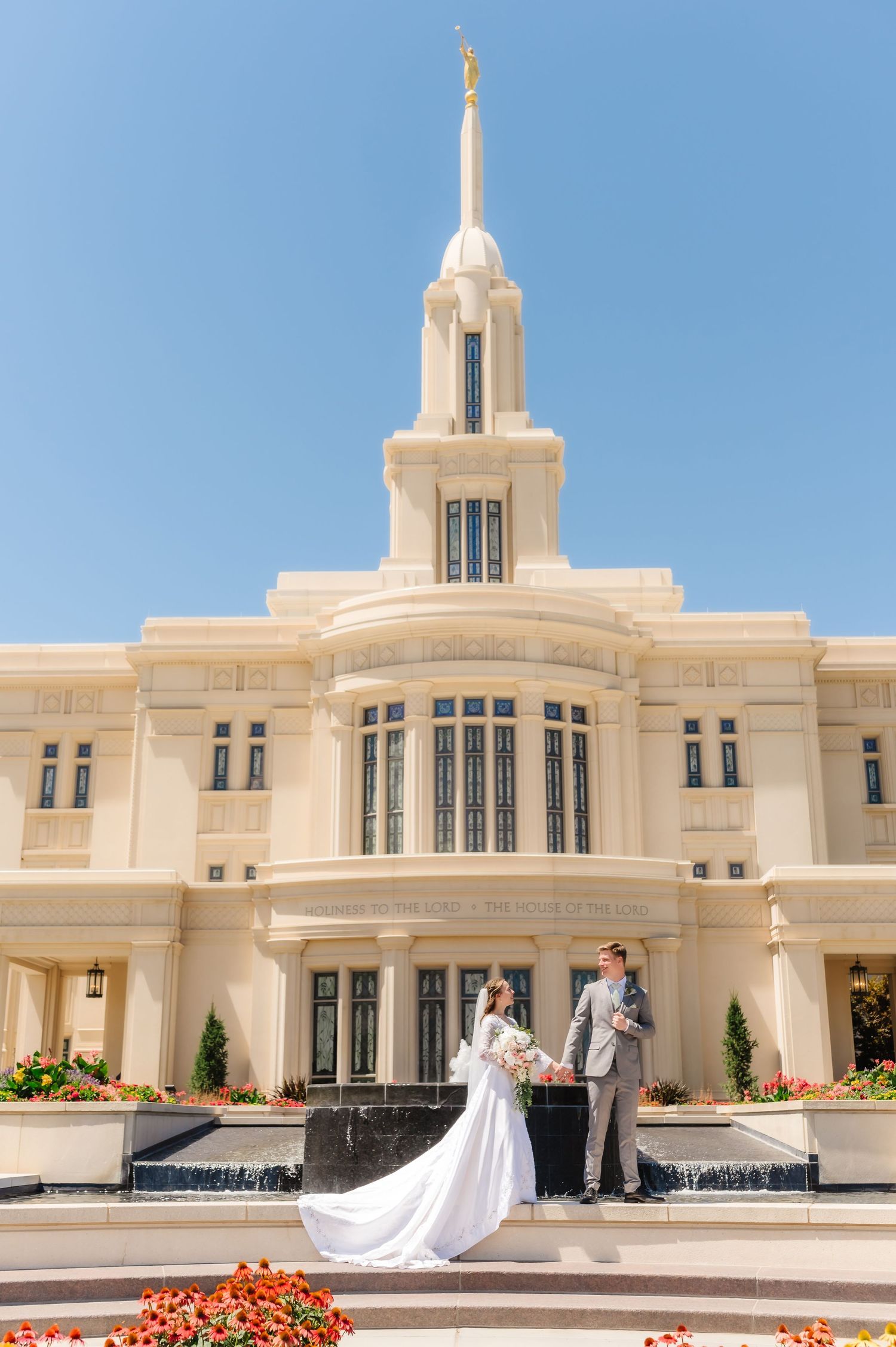 Elegant white temple building with spires and fountains against a bright blue sky.