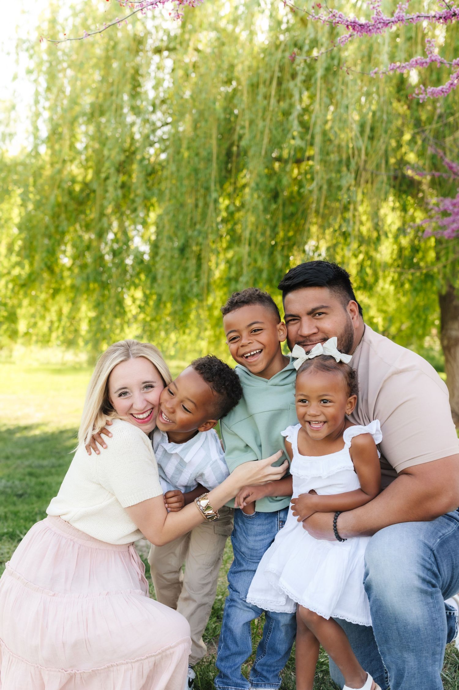 Family members share warm embraces and laughter while sitting together outdoors under flowering trees.