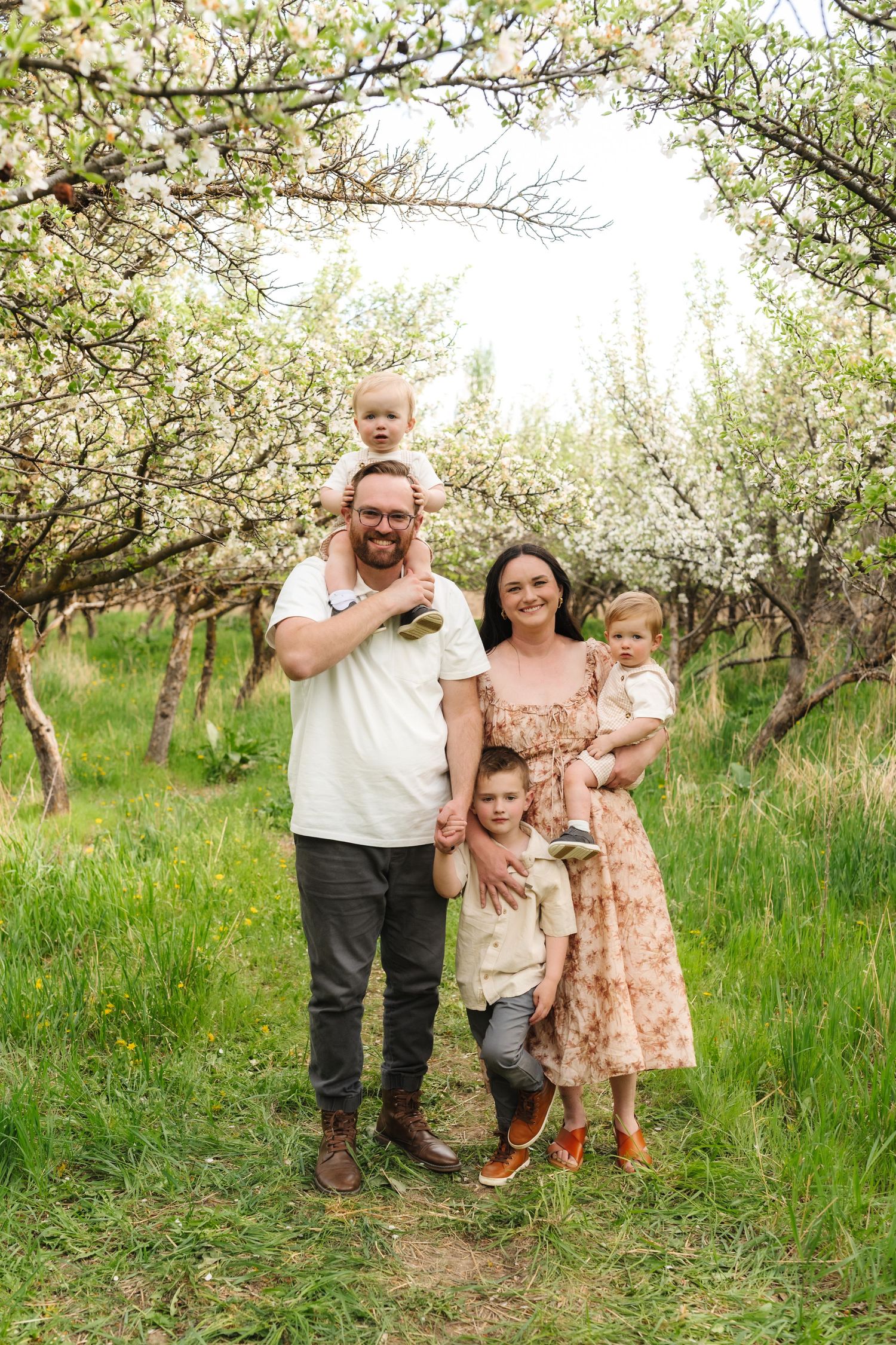 A family stands together in a blooming spring orchard with white blossoms and green grass.