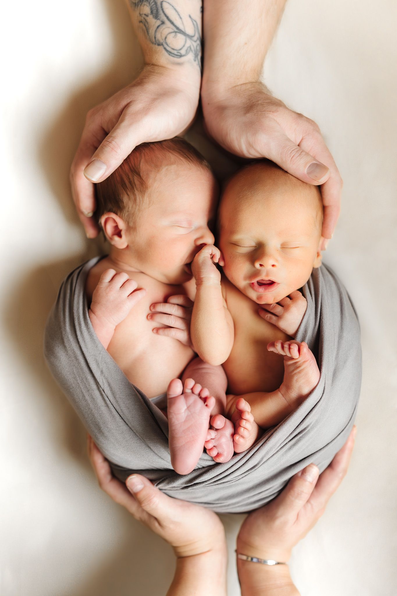 Twin babies sleeping peacefully together wrapped in soft grey fabric.