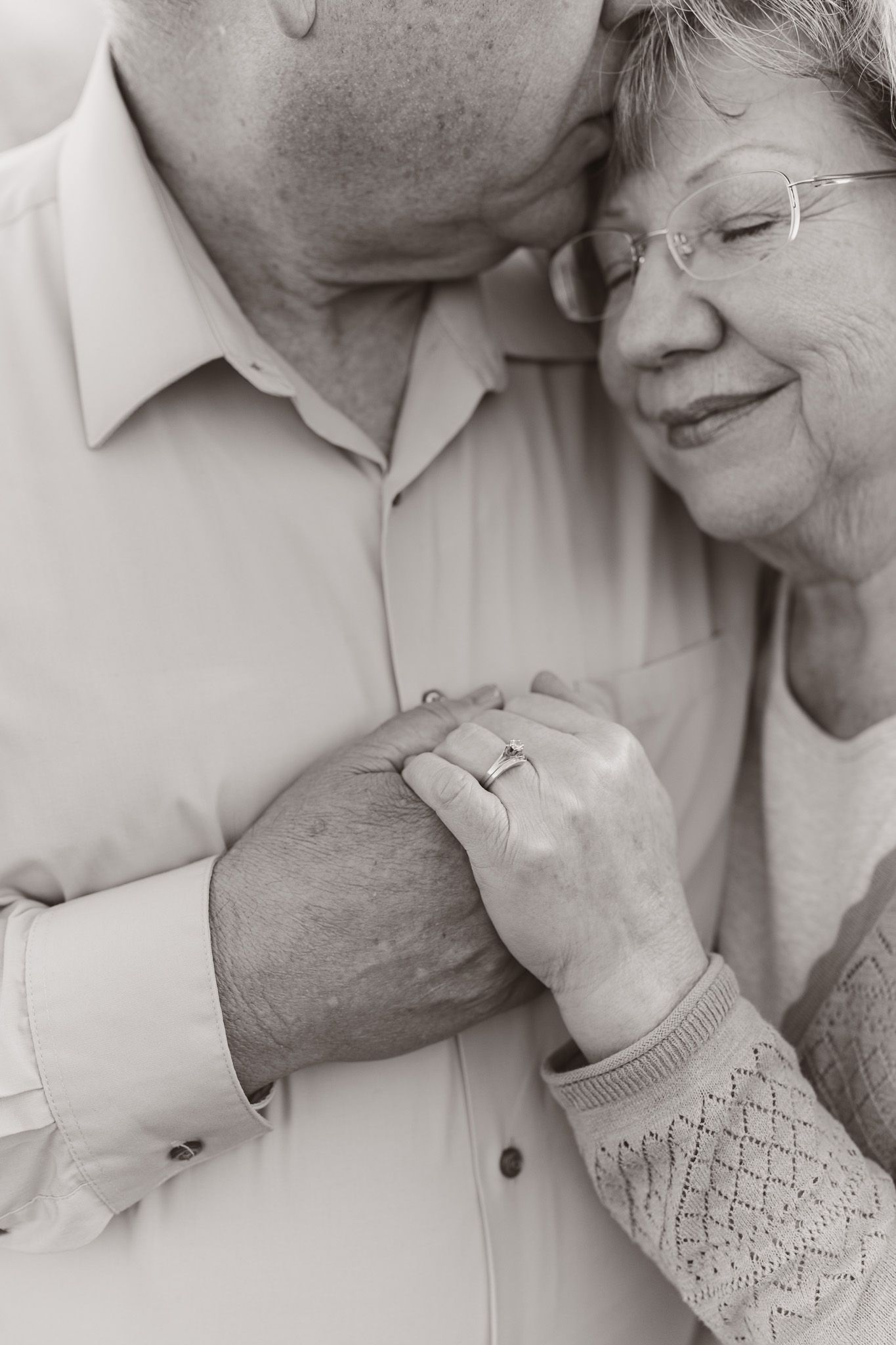 Intimate black and white close-up showing tender embrace between elderly couple with clasped hands.