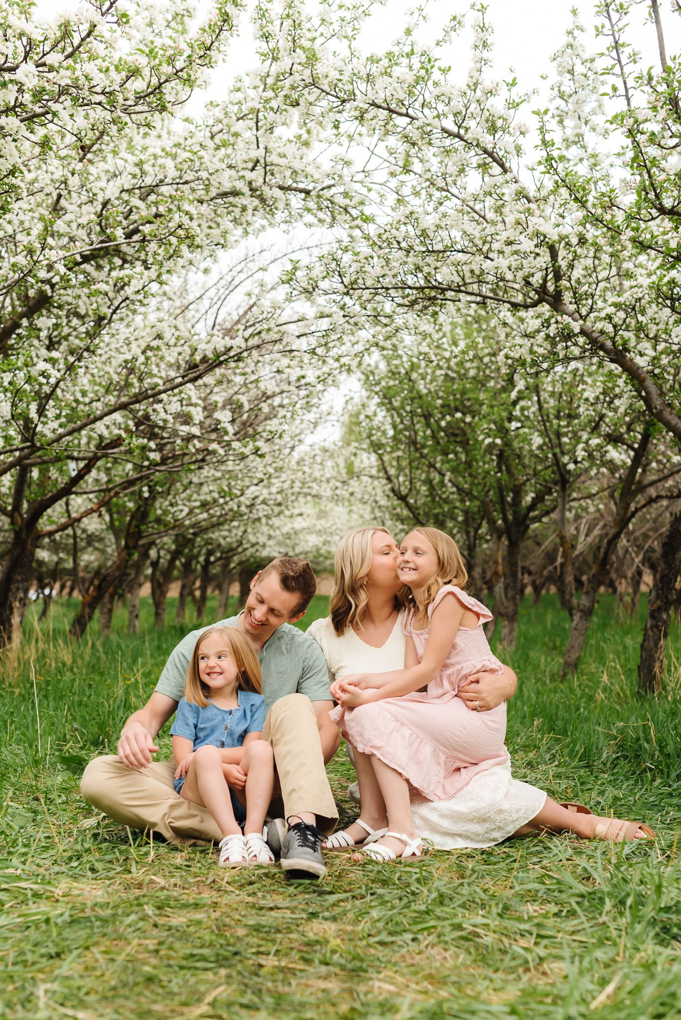 Family lying together in a blooming spring orchard during golden hour photo session.