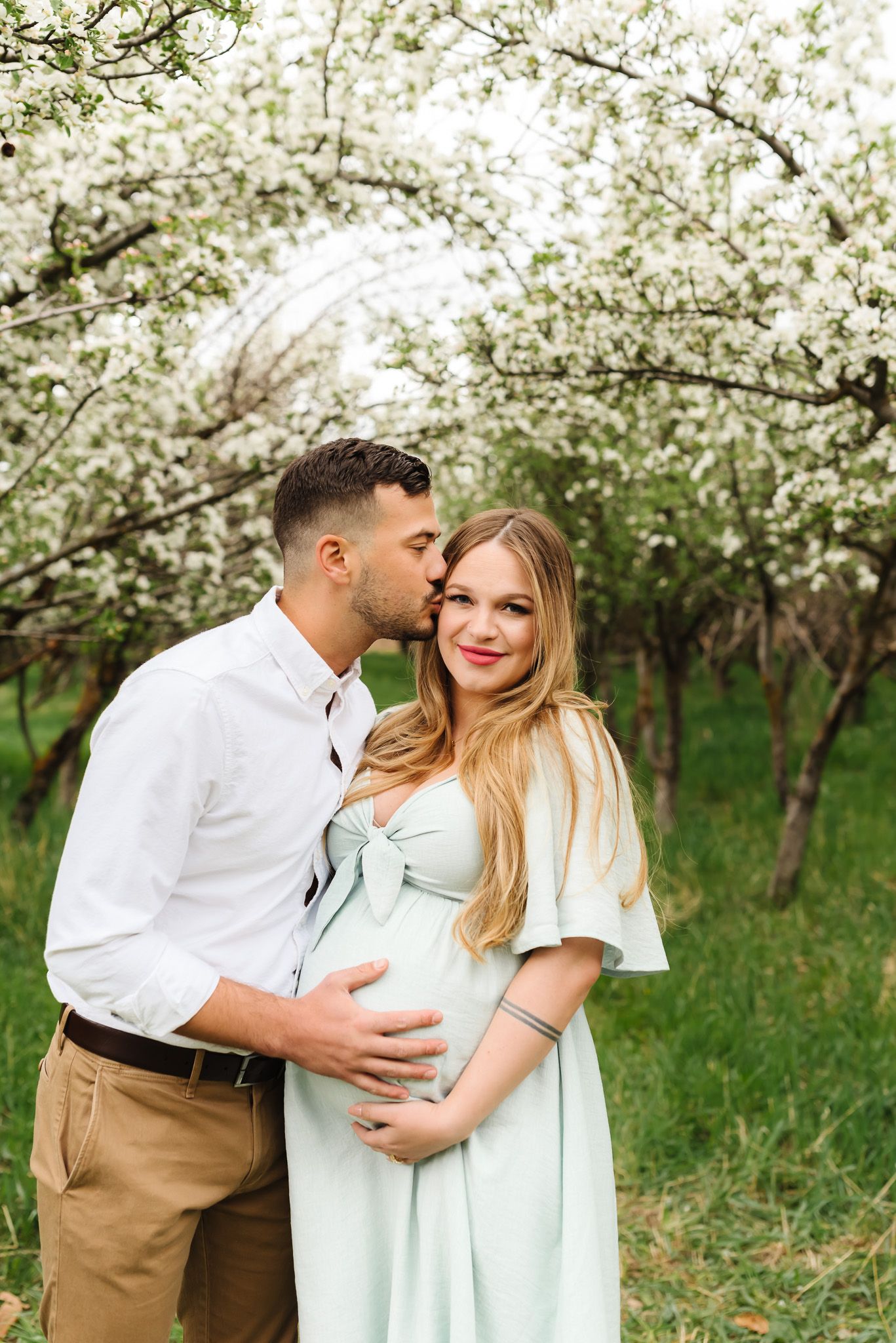 Romantic couple embracing in springtime orchard with white blossoming trees.