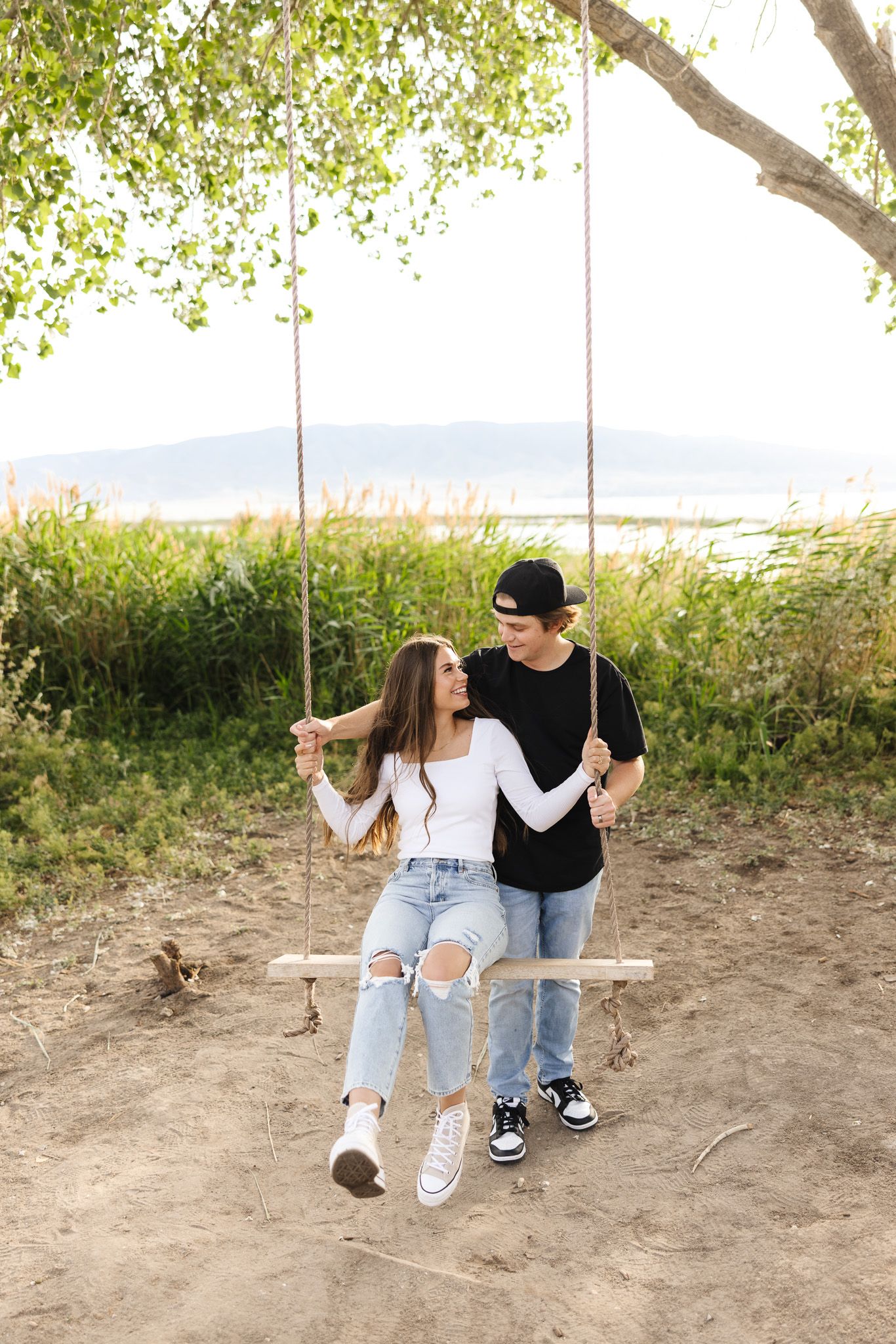 A couple sits together on a wooden swing in a natural outdoor setting surrounded by greenery.
