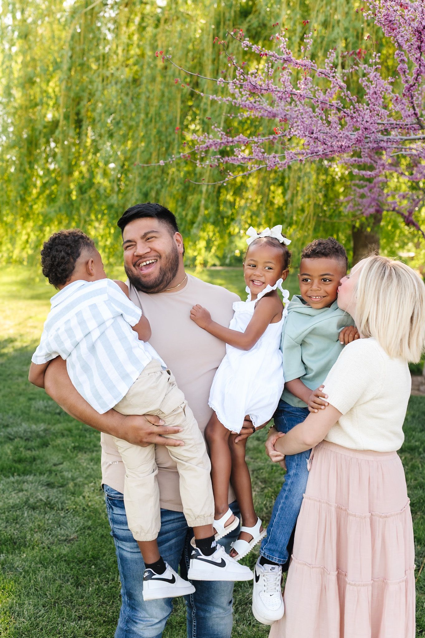 Happy interracial family with three young children enjoying a sunny day outdoors near a blooming pink tree.