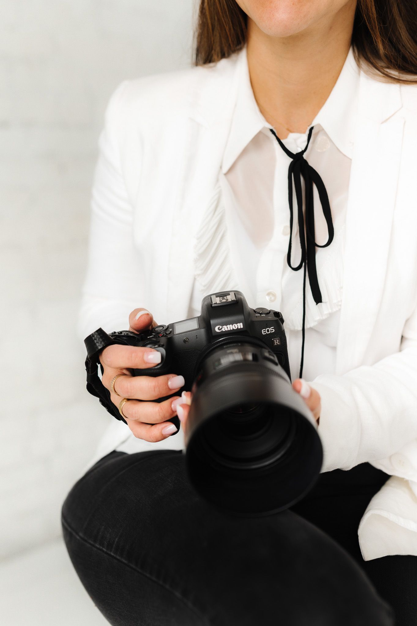 Close-up of hands holding professional camera while wearing white blazer and black tie.